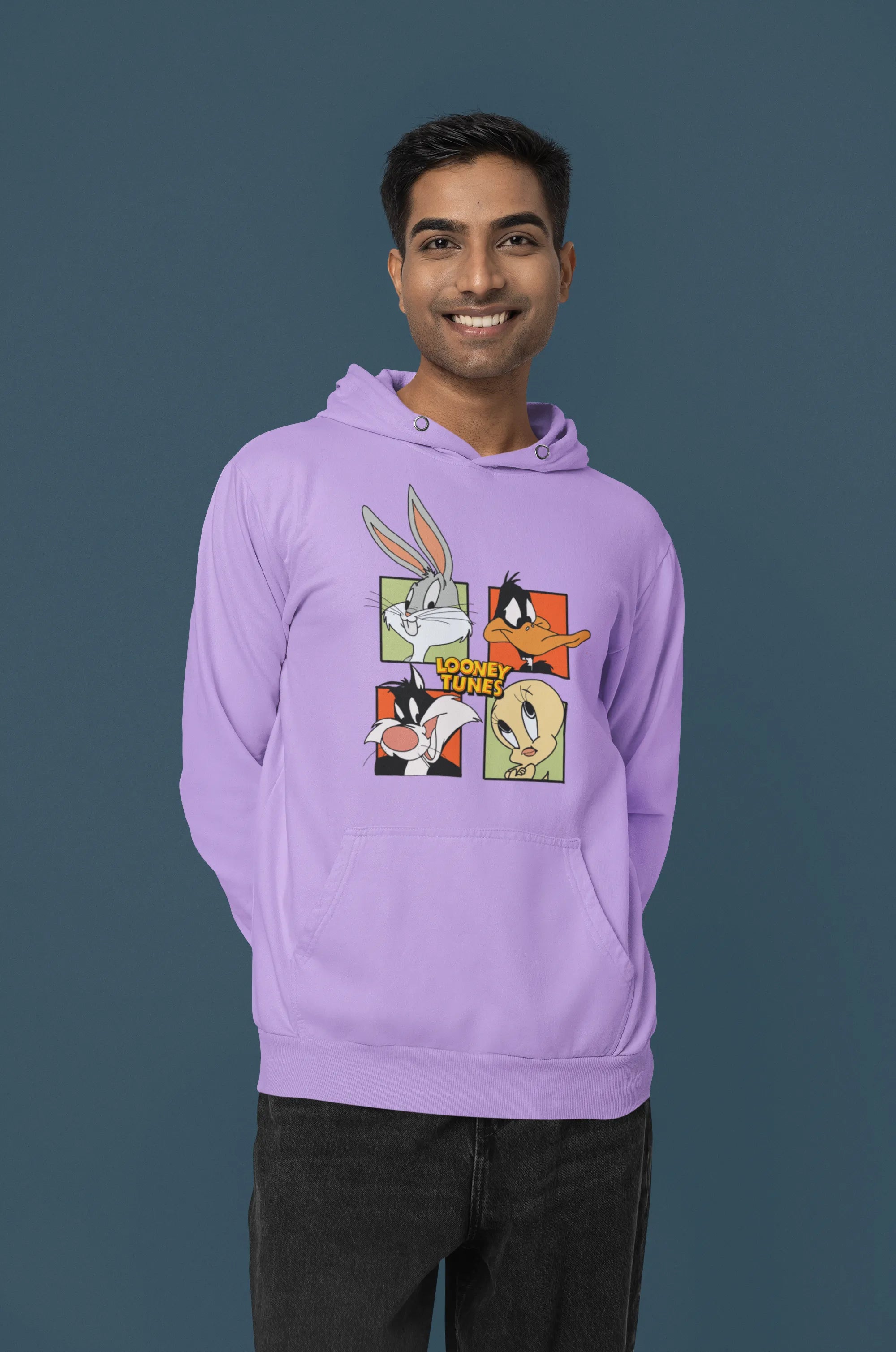 Third image of a male model wearing a lavender hoodie with a large Looney Tunes design. The illustration features portraits of several iconic Looney Tunes characters.