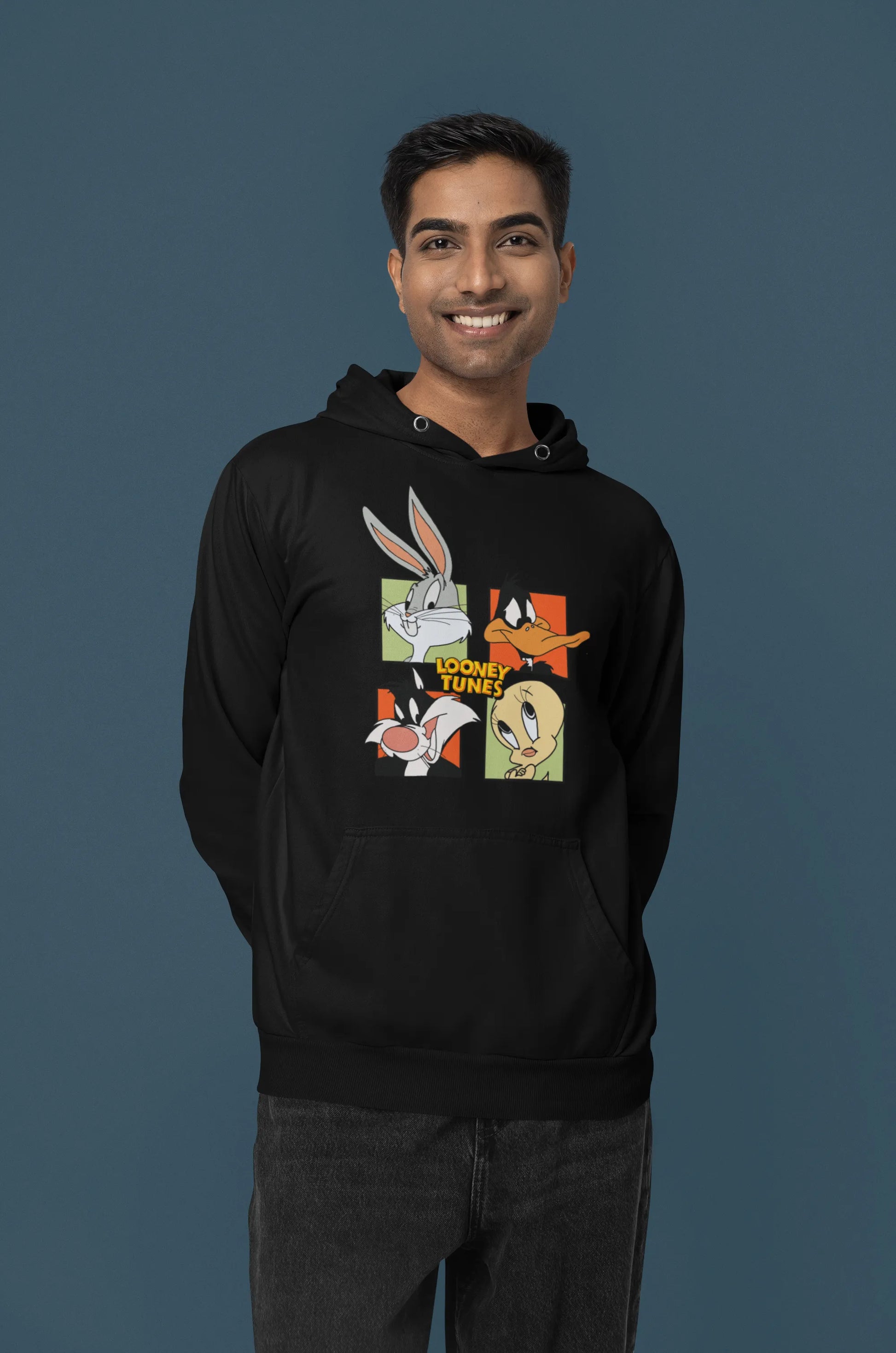 Third image of a male model wearing a black hoodie with a large Looney Tunes design. The illustration features portraits of several iconic Looney Tunes characters.