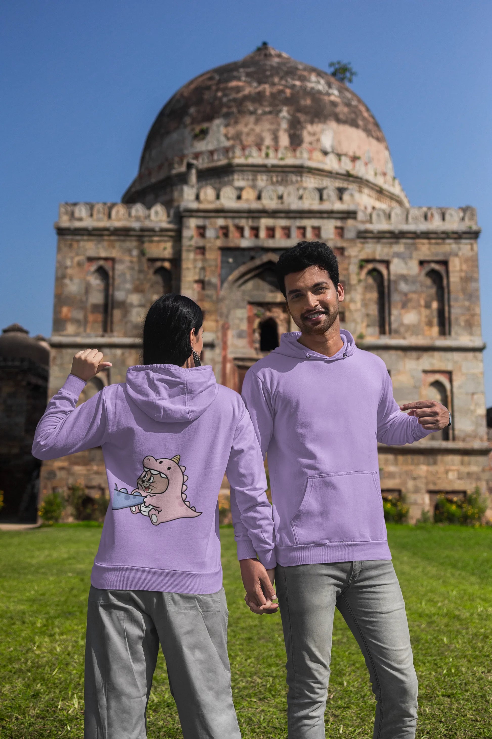 Second back and front view of a couple wearing matching lavender hoodies, one with Tom the cat and the other with Jerry the mouse, both dressed in dinosaur costumes.