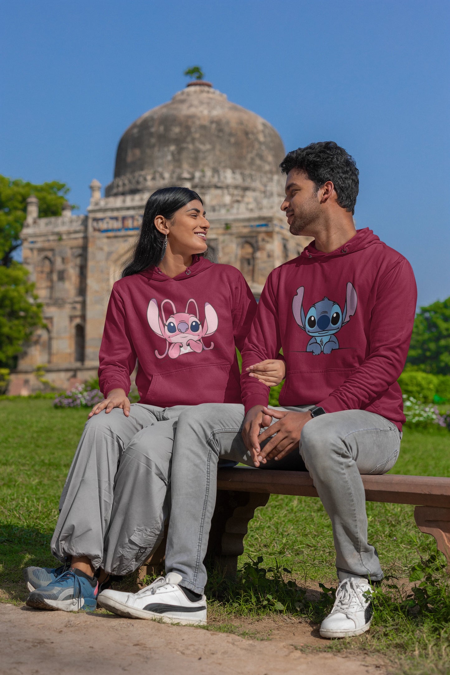 2nd front view of a couple wearing matching maroon hoodies, one with a Stitch design and the other with an Angel design.