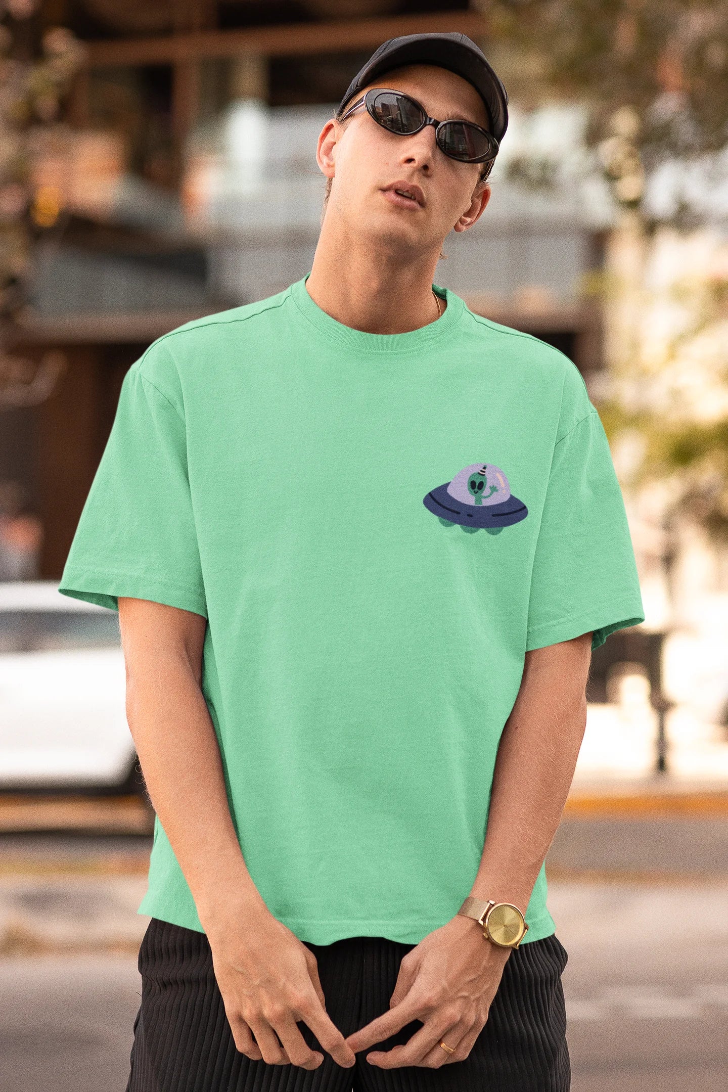 First front view of a male model wearing a mint green oversized t-shirt featuring a fun "Alienated" design with elements of spaceships, UFOs, and a hint of extraterrestrial life.