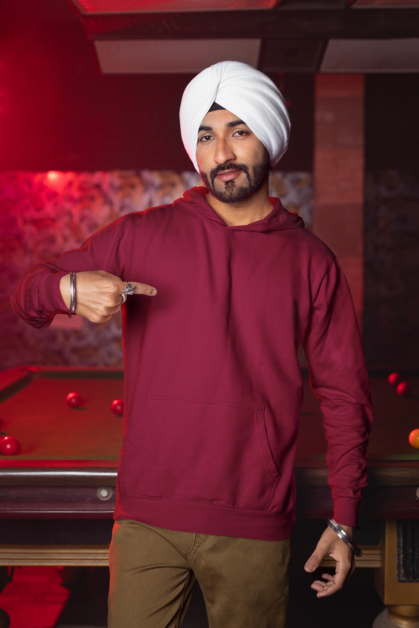 Second front view of a male model wearing a maroon hoodie with a portrait of Diljit Dosanjh and lyrics from the song "Ikk Kudi."