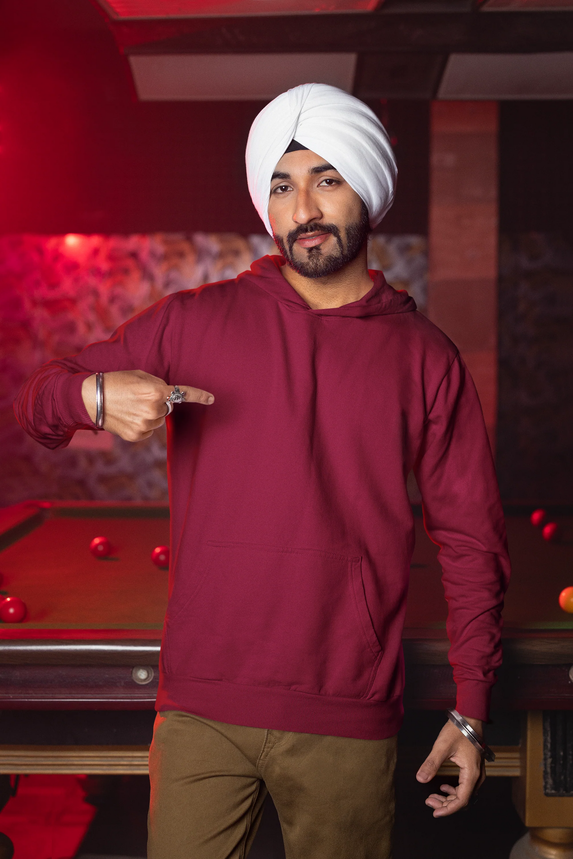 Second front view of a male model wearing a maroon hoodie with a portrait of Diljit Dosanjh and lyrics from the song "Ikk Kudi."
