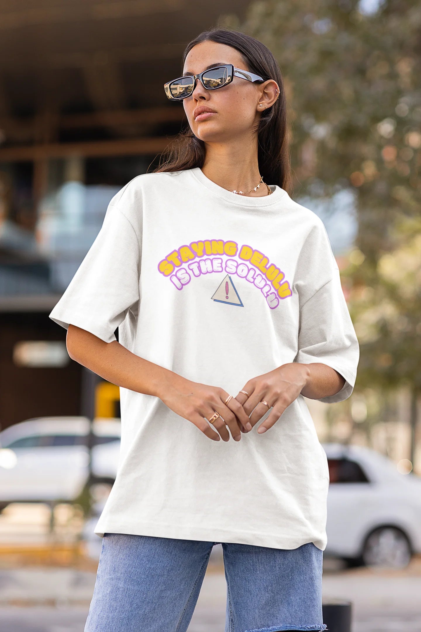 Side view of female model wearing an off-white oversized t-shirt with the hilarious message "Stay Delulu" in a bold design. Ideal for those who love trendy slang and lighthearted humor. 