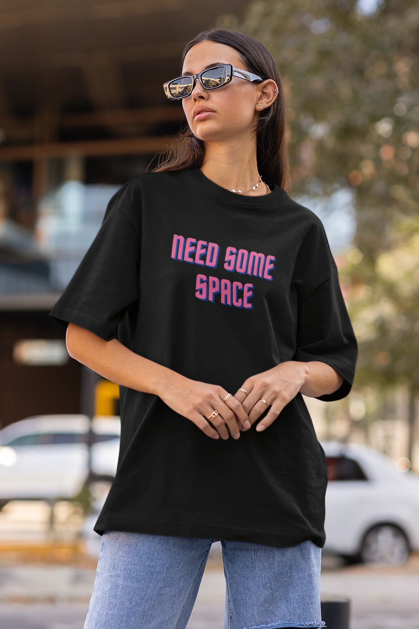 Side view of a female model wearing a black oversized t-shirt with a bold graphic that reads "Need Some Space" on the front. The design incorporates subtle hints of the Milky Way galaxy and the solar system on the back.