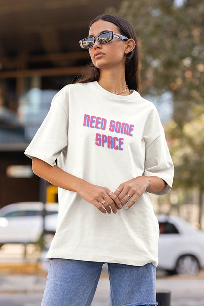 Side view of a female model wearing a white oversized t-shirt with a bold graphic that reads "Need Some Space" on the front. The design incorporates subtle hints of the Milky Way galaxy and the solar system on the back.