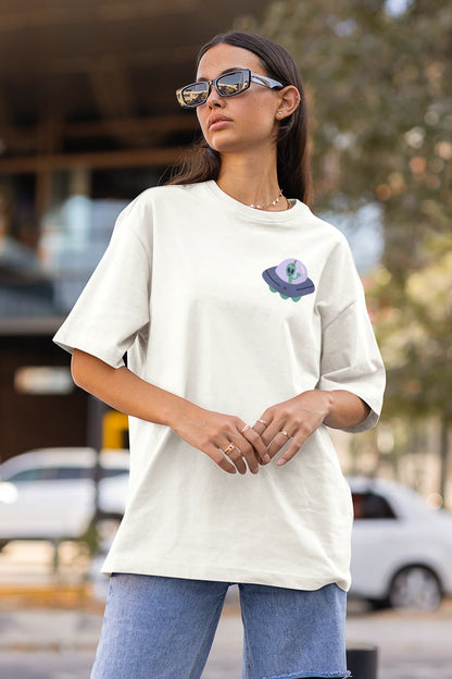 Side view of a female model wearing a off-white oversized t-shirt featuring a fun "Alienated" design with elements of spaceships, UFOs, and a hint of extraterrestrial life.