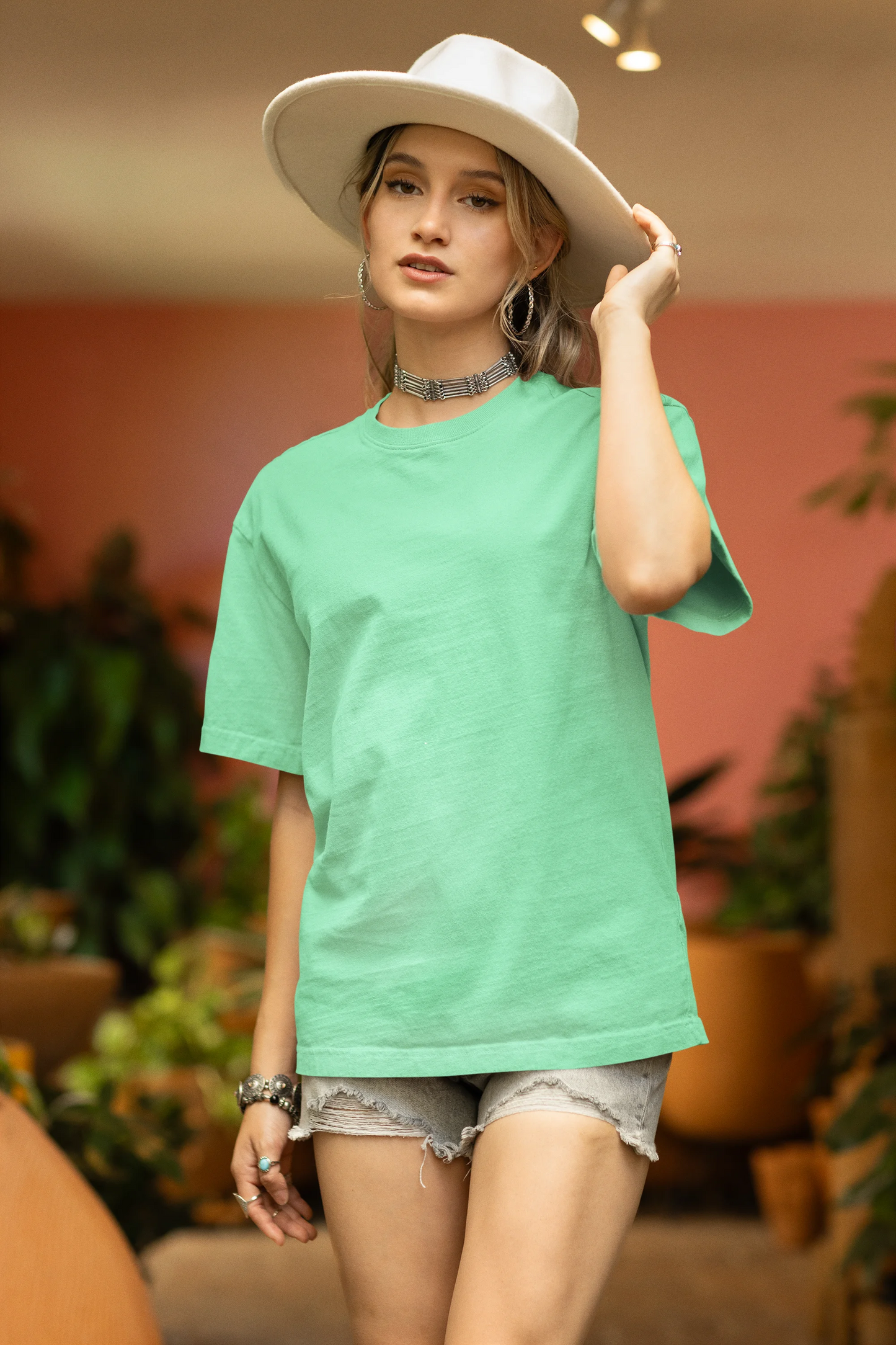 Front view of a female model wearing a mint green oversized t-shirt featuring a nature-inspired design with a blue dragonfly perched on flowers amidst green grass. Ideal for those who love springtime aesthetics and dragonfly imagery.