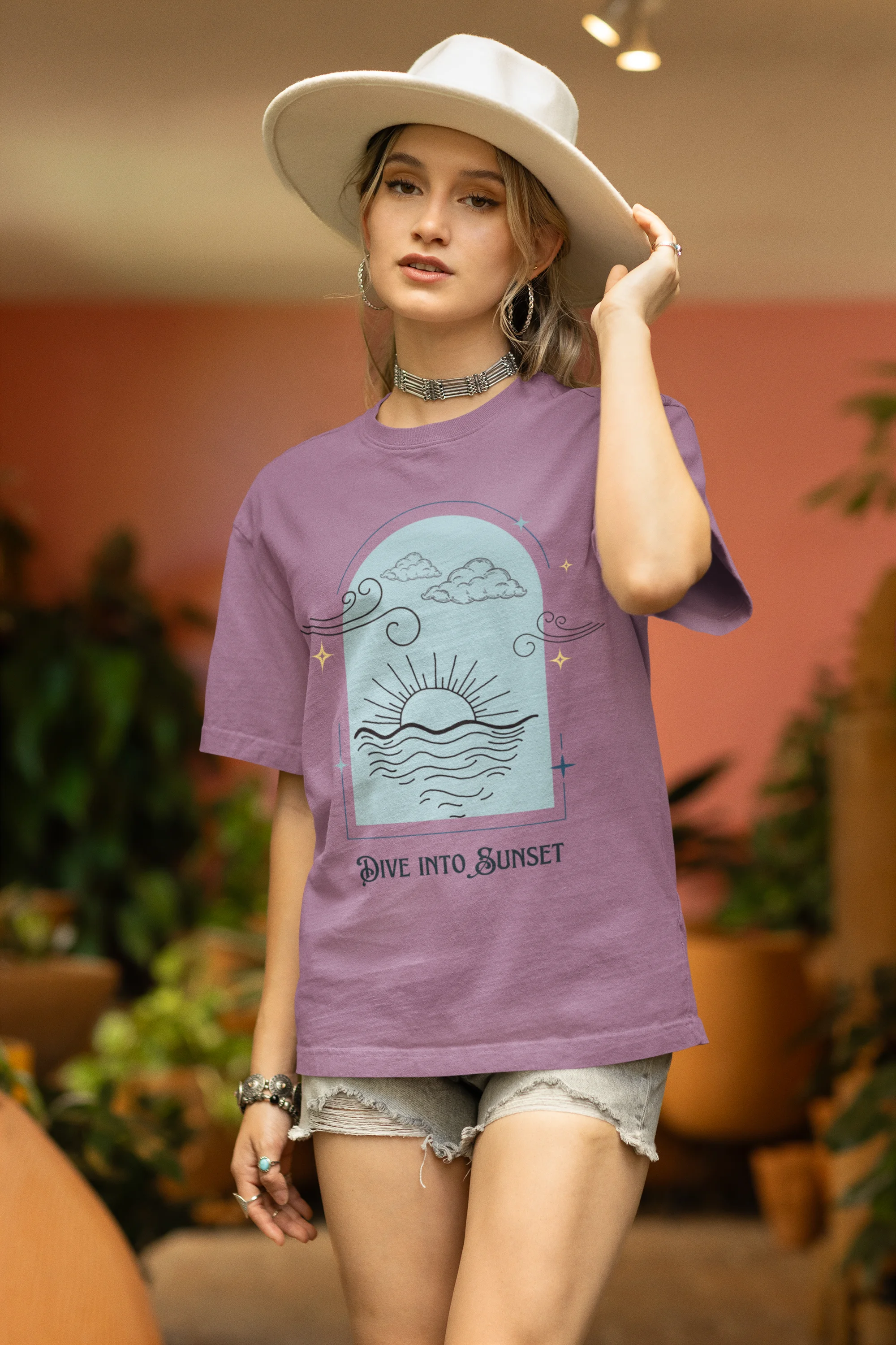 Side view of a female model wearing a dirty purple oversized t-shirt with a beautiful outline of the sun setting into the sea, offering a serene and coastal aesthetic.