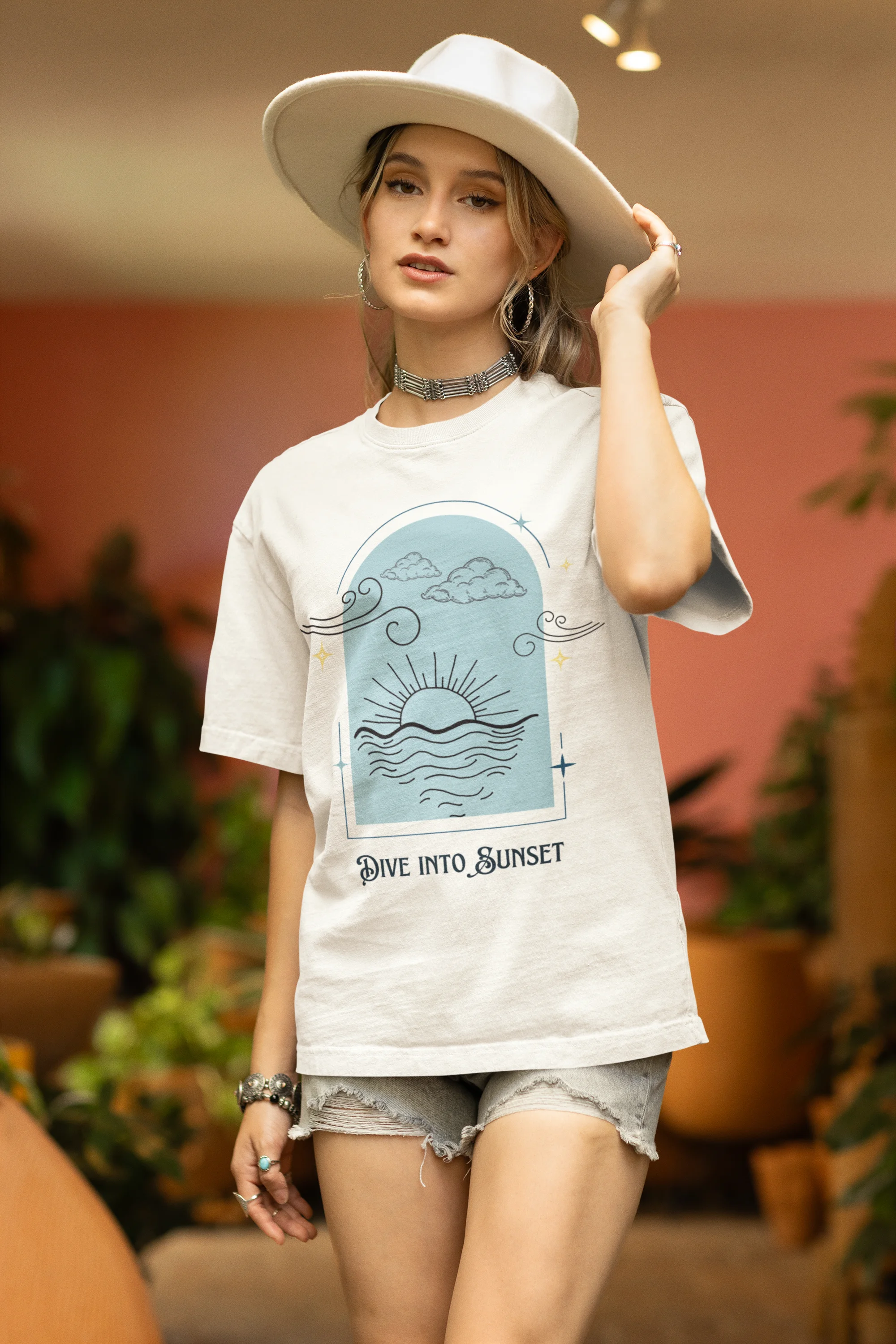 Side view of a female model wearing a off-white oversized t-shirt with a beautiful outline of the sun setting into the sea, offering a serene and coastal aesthetic.