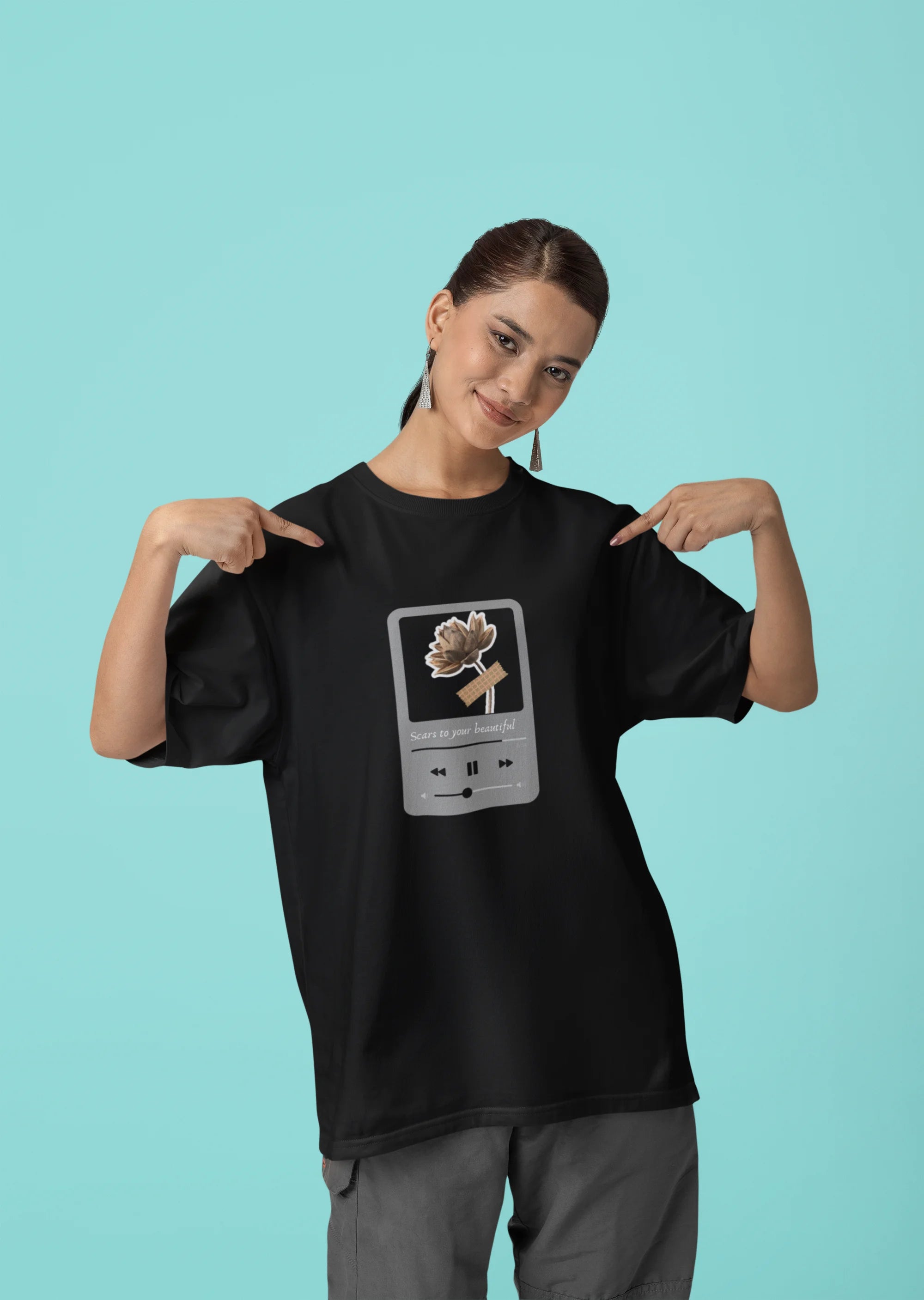 First front view of a female model wearing a black oversized t-shirt featuring a design inspired by Alessia Cara's song "Scars to Your Beautiful." The design includes flowers and a message of self-love. Ideal for fans of Alessia Cara and those who appreciate messages of empowerment.