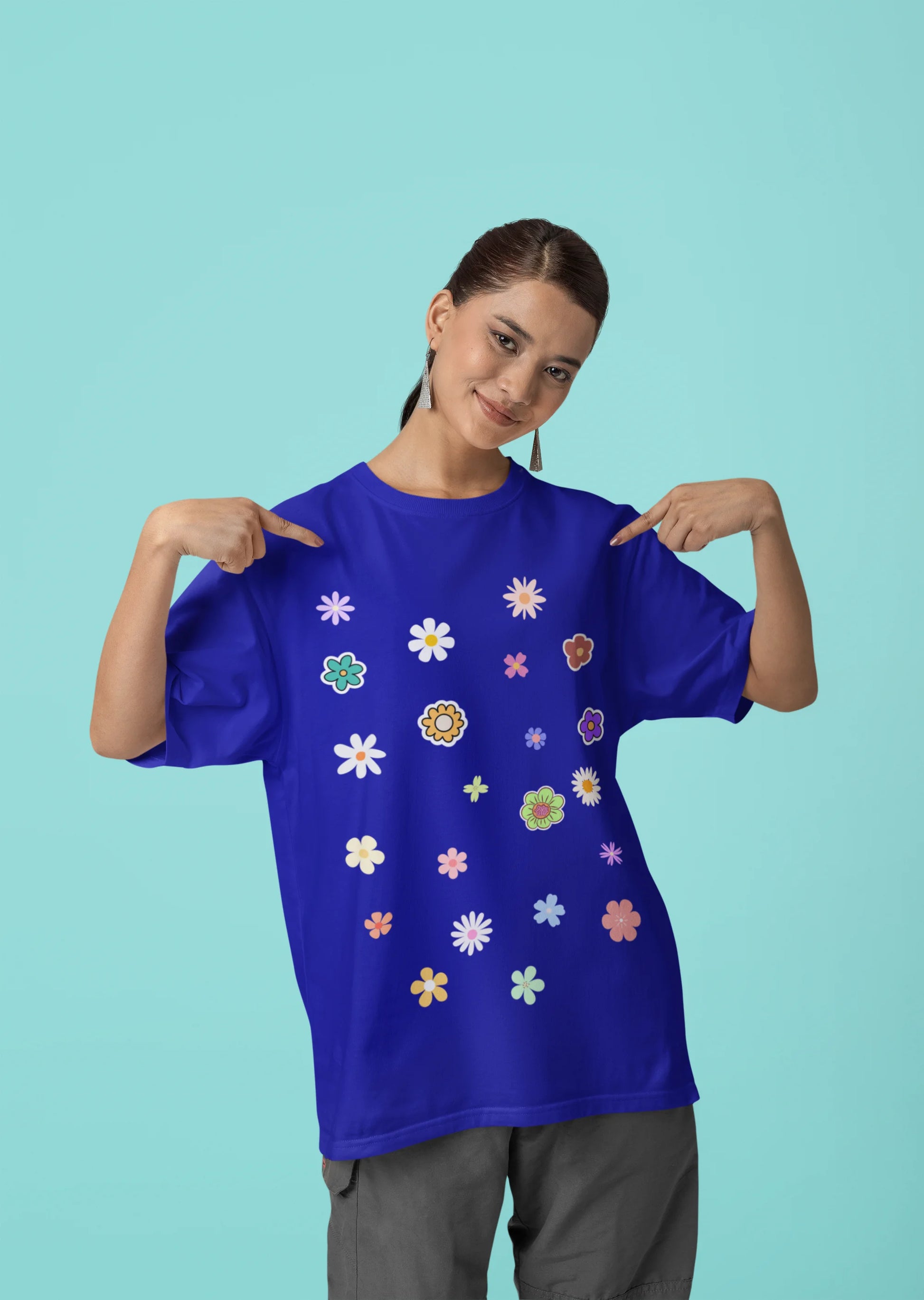 Female model pointing to a royal blue oversized t-shirt featuring a vibrant floral design with roses, tulips, sunflowers, and orchids. Ideal for those who love floral patterns and spring fashion.