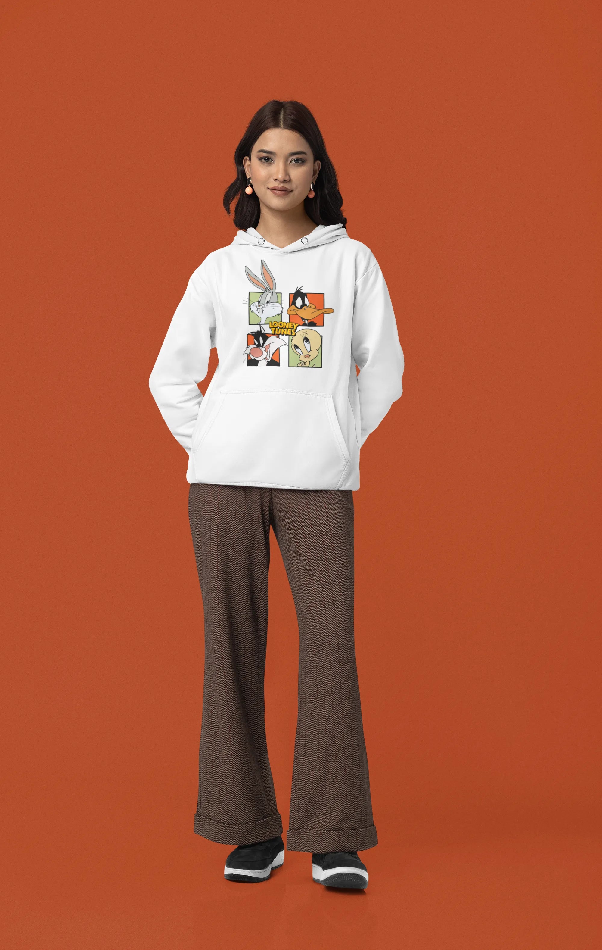 Fourth image of a female model wearing a white hoodie with a large Looney Tunes design. The illustration features portraits of several iconic Looney Tunes characters.