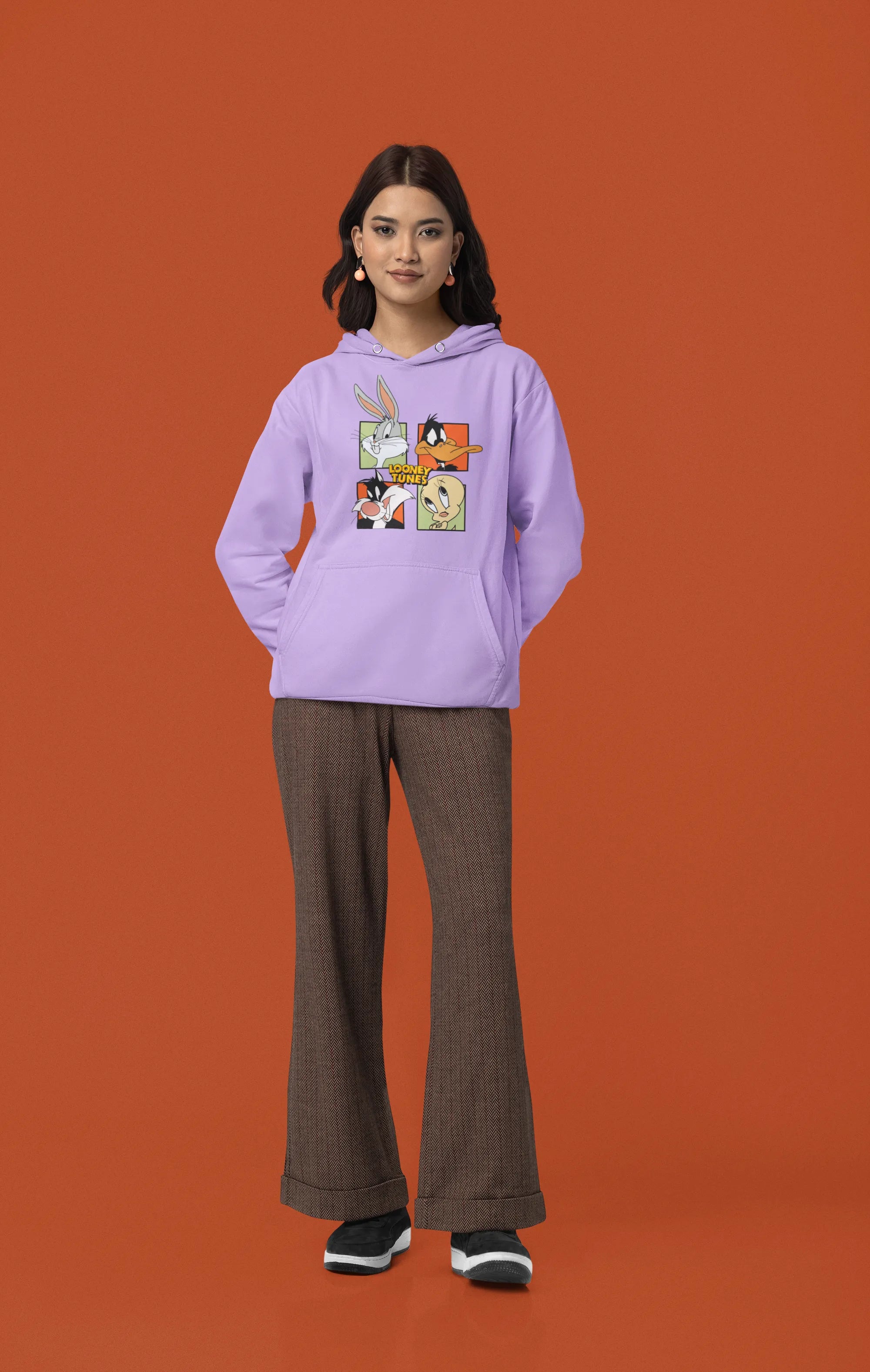 Fourth image of a female model wearing a lavender hoodie with a large Looney Tunes design. The illustration features portraits of several iconic Looney Tunes characters.