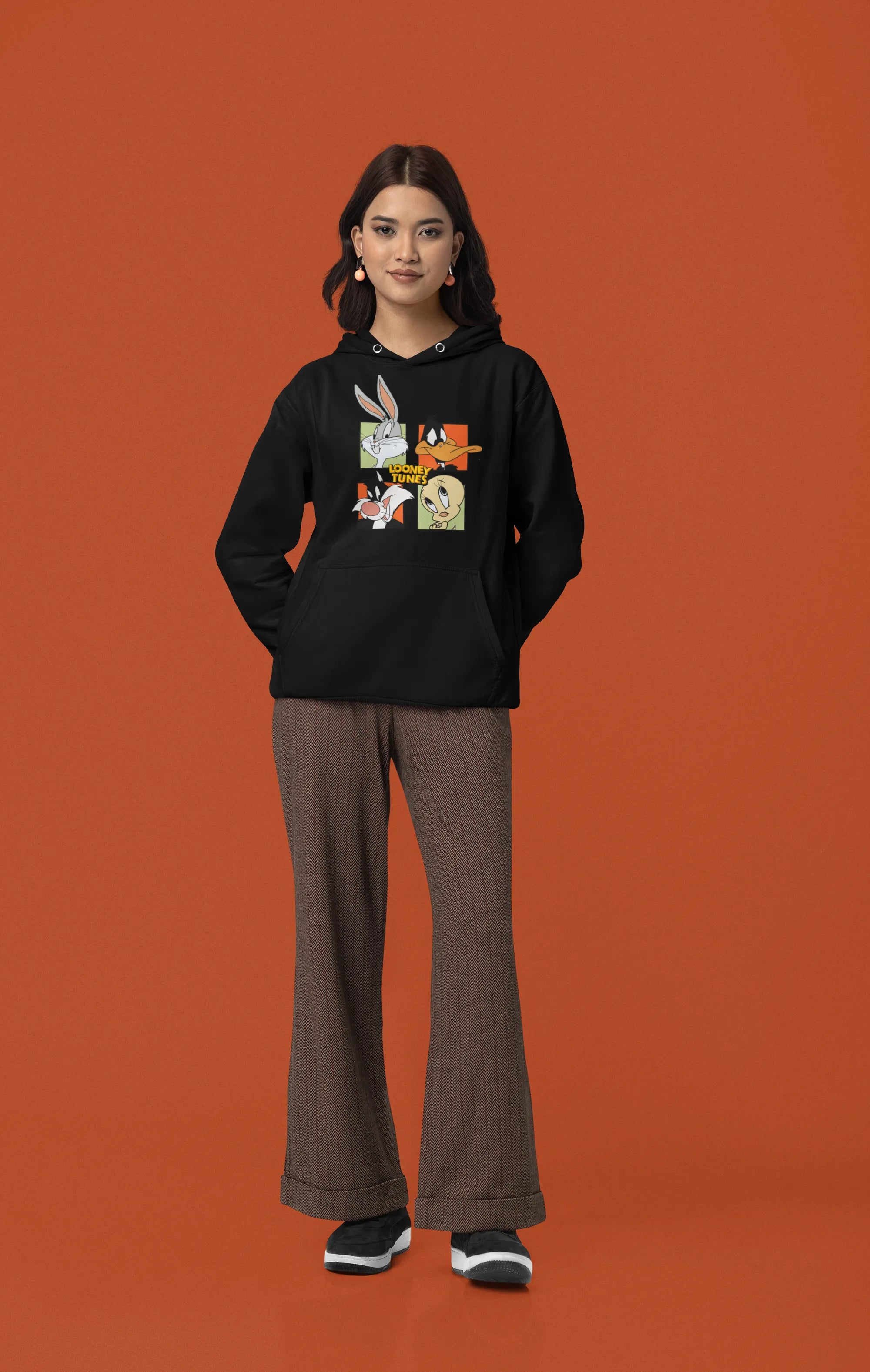 Third image of a female model wearing a black hoodie with a large Looney Tunes design. The illustration features portraits of several iconic Looney Tunes characters.