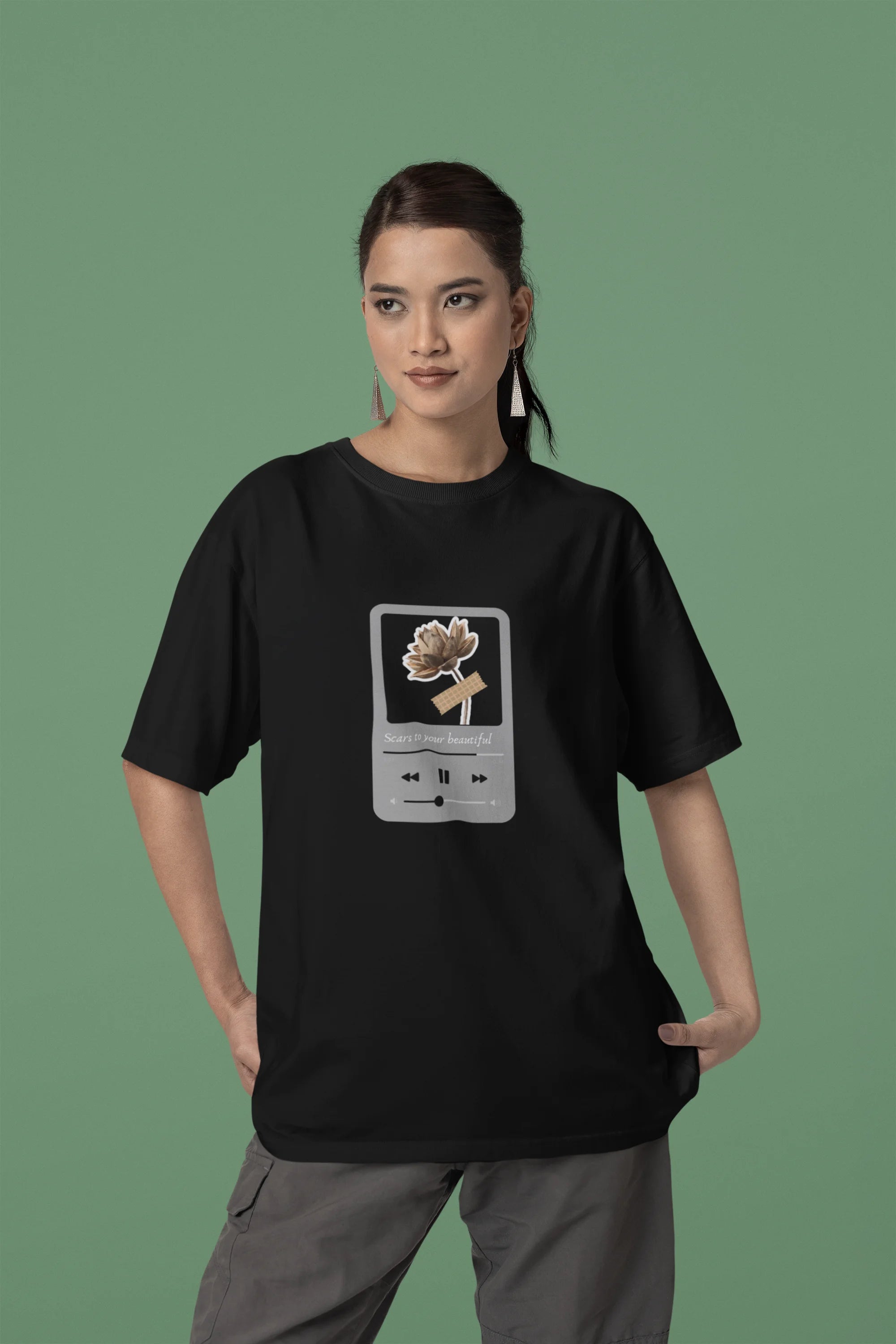 Second front view of a female model wearing a black oversized t-shirt featuring a design inspired by Alessia Cara's song "Scars to Your Beautiful." The design includes flowers and a message of self-love. Ideal for fans of Alessia Cara and those who appreciate messages of empowerment.