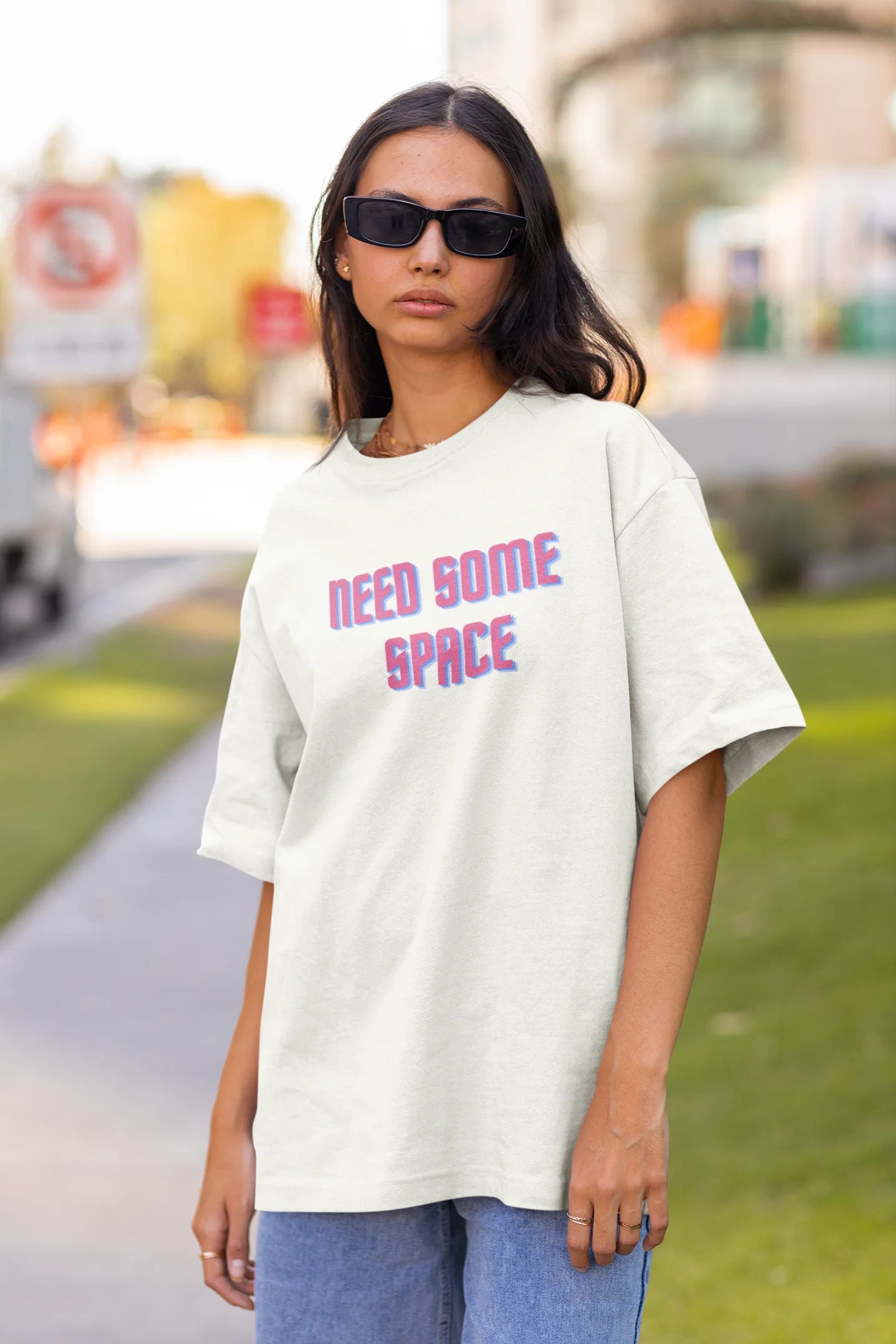 Front view of a female model wearing a white oversized t-shirt with a bold graphic that reads "Need Some Space" on the front. The design incorporates subtle hints of the Milky Way galaxy and the solar system on the back.