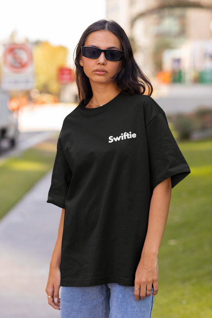 Front view of female model flaunting Taylor Swift-themed black oversized tee, epitomizing rockstar chic with nods to Taylor's Version and Eras Tour.