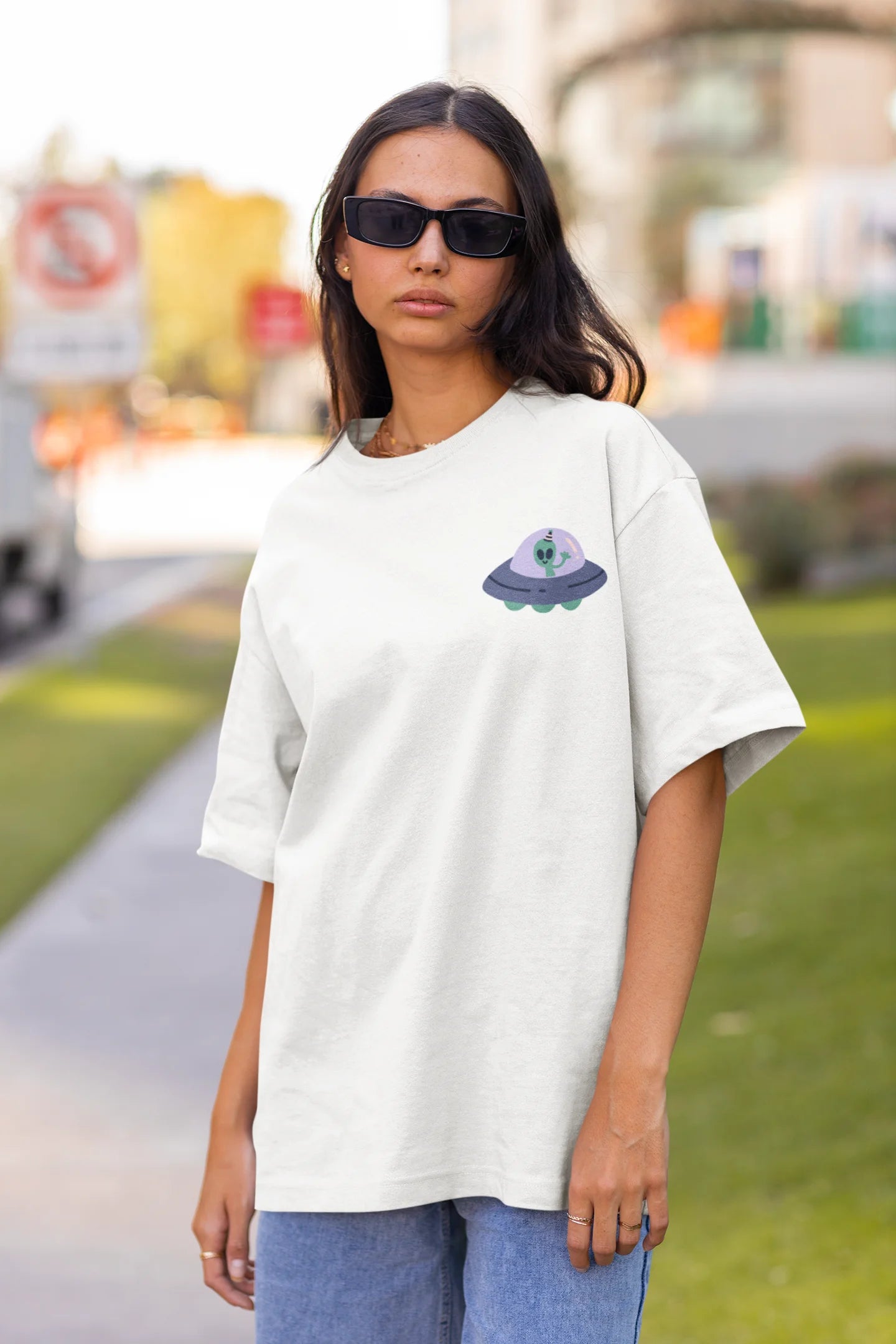 Front view of a female model wearing a off-white oversized t-shirt featuring a fun "Alienated" design with elements of spaceships, UFOs, and a hint of extraterrestrial life.