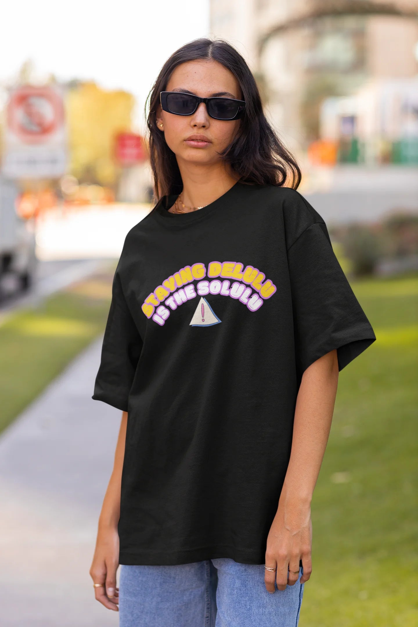 Front view of female model wearing a black oversized t-shirt with the hilarious message "Stay Delulu" in a bold design. Ideal for those who love trendy slang and lighthearted humor. 