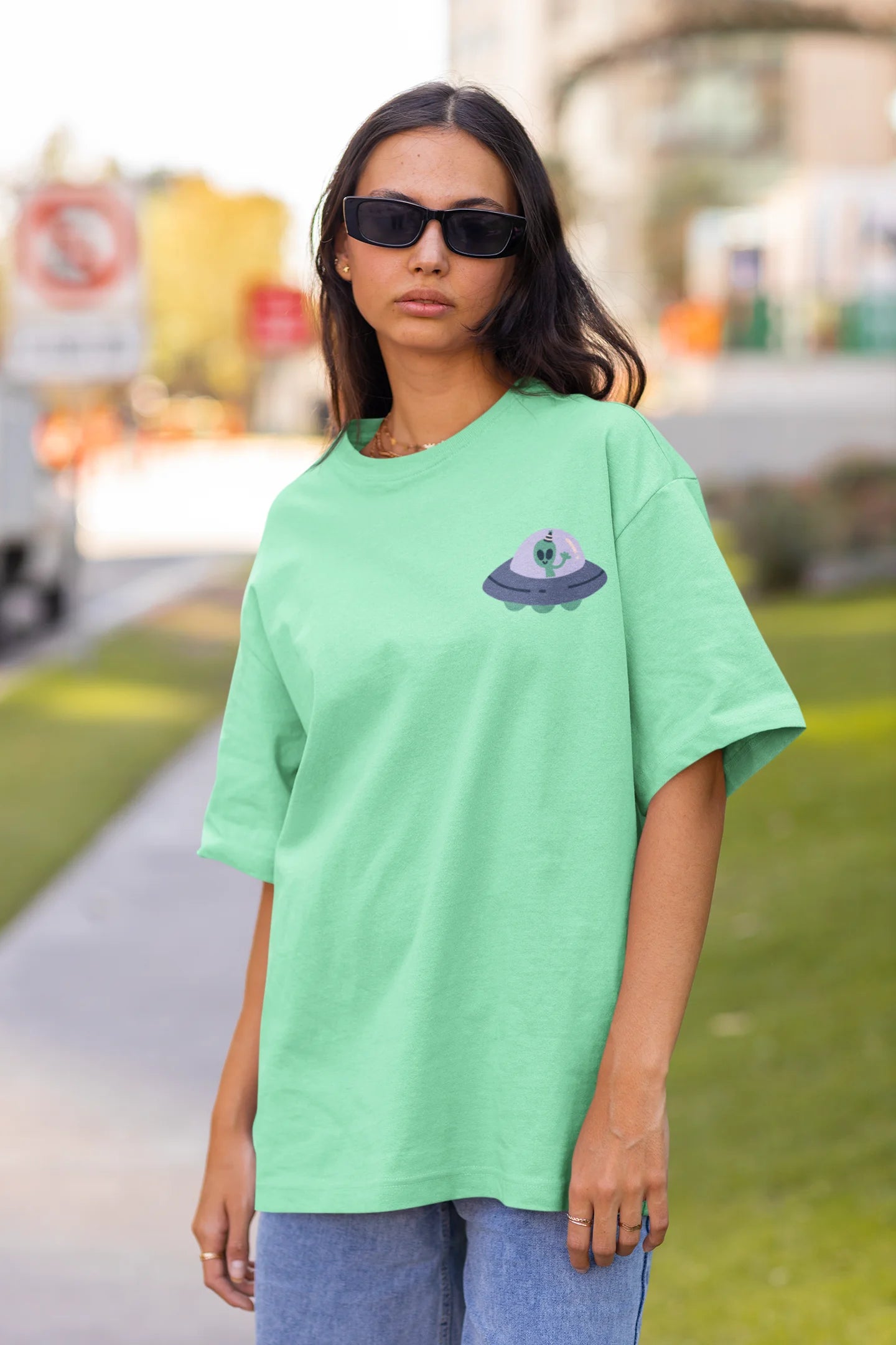 Front view of a female model wearing a mint green oversized t-shirt featuring a fun "Alienated" design with elements of spaceships, UFOs, and a hint of extraterrestrial life.