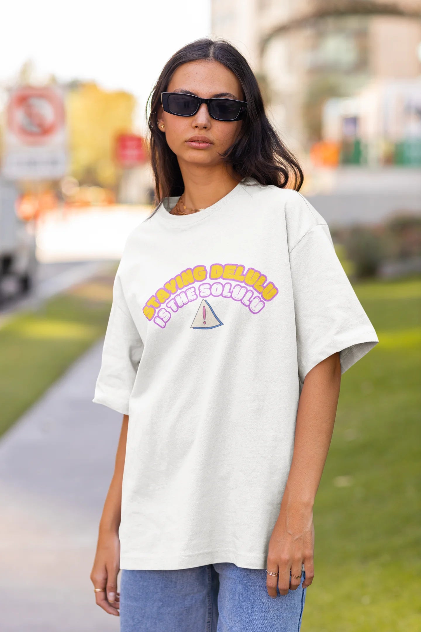 Front view of female model wearing an off-white oversized t-shirt with the hilarious message "Stay Delulu" in a bold design. Ideal for those who love trendy slang and lighthearted humor. 