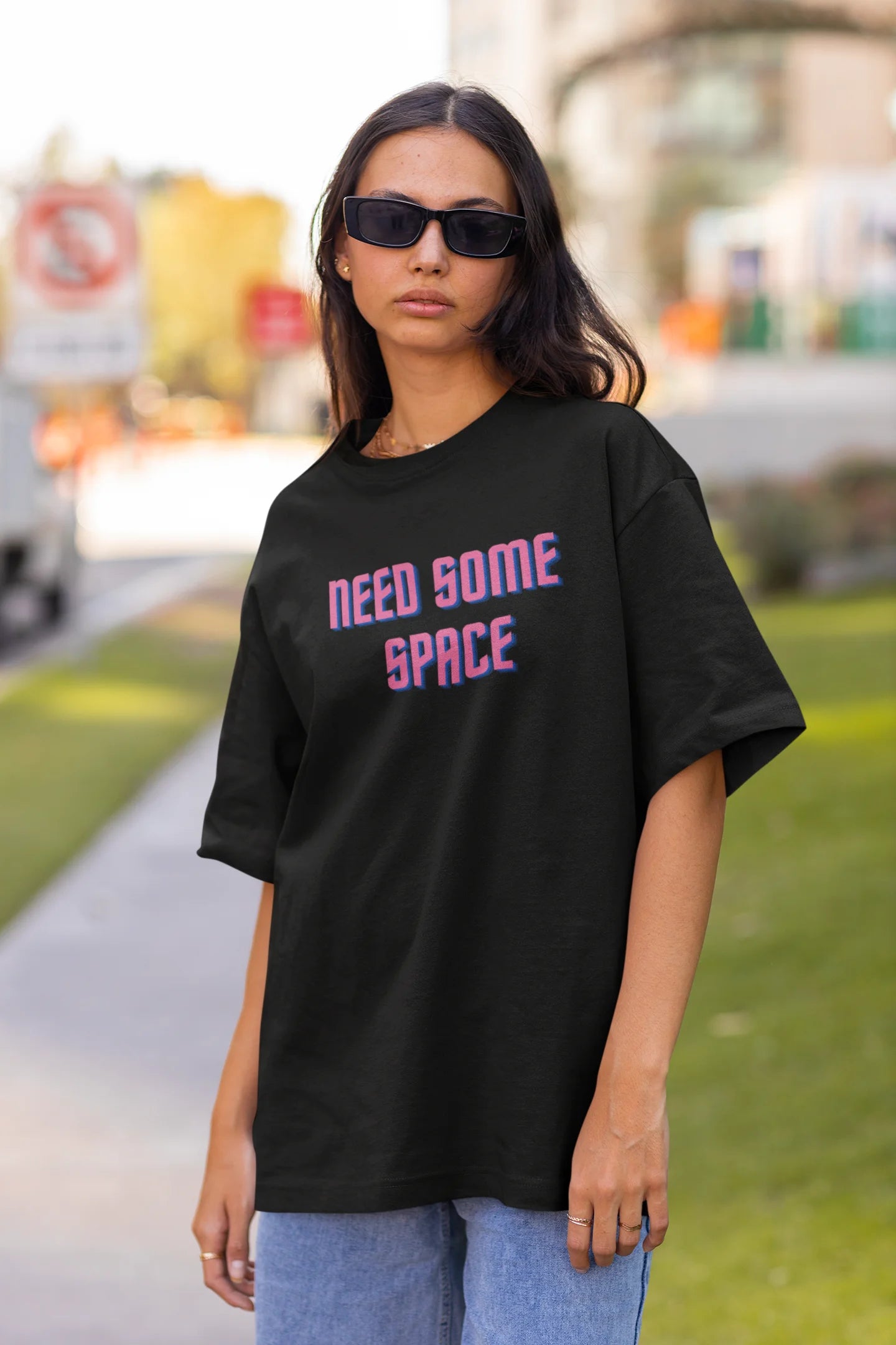 Front view of a female model wearing a black oversized t-shirt with a bold graphic that reads "Need Some Space" on the front. The design incorporates subtle hints of the Milky Way galaxy and the solar system on the back.
