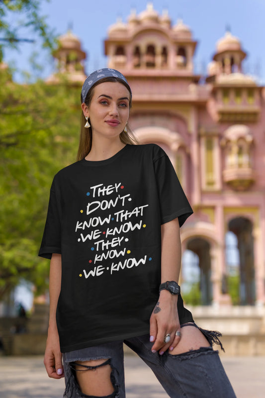 First image of female model wearing black oversized t-shirt with F.R.I.E.N.D.S series inspired designs, embodying Phoebe's unique humor with the quote 'They Know We Know'