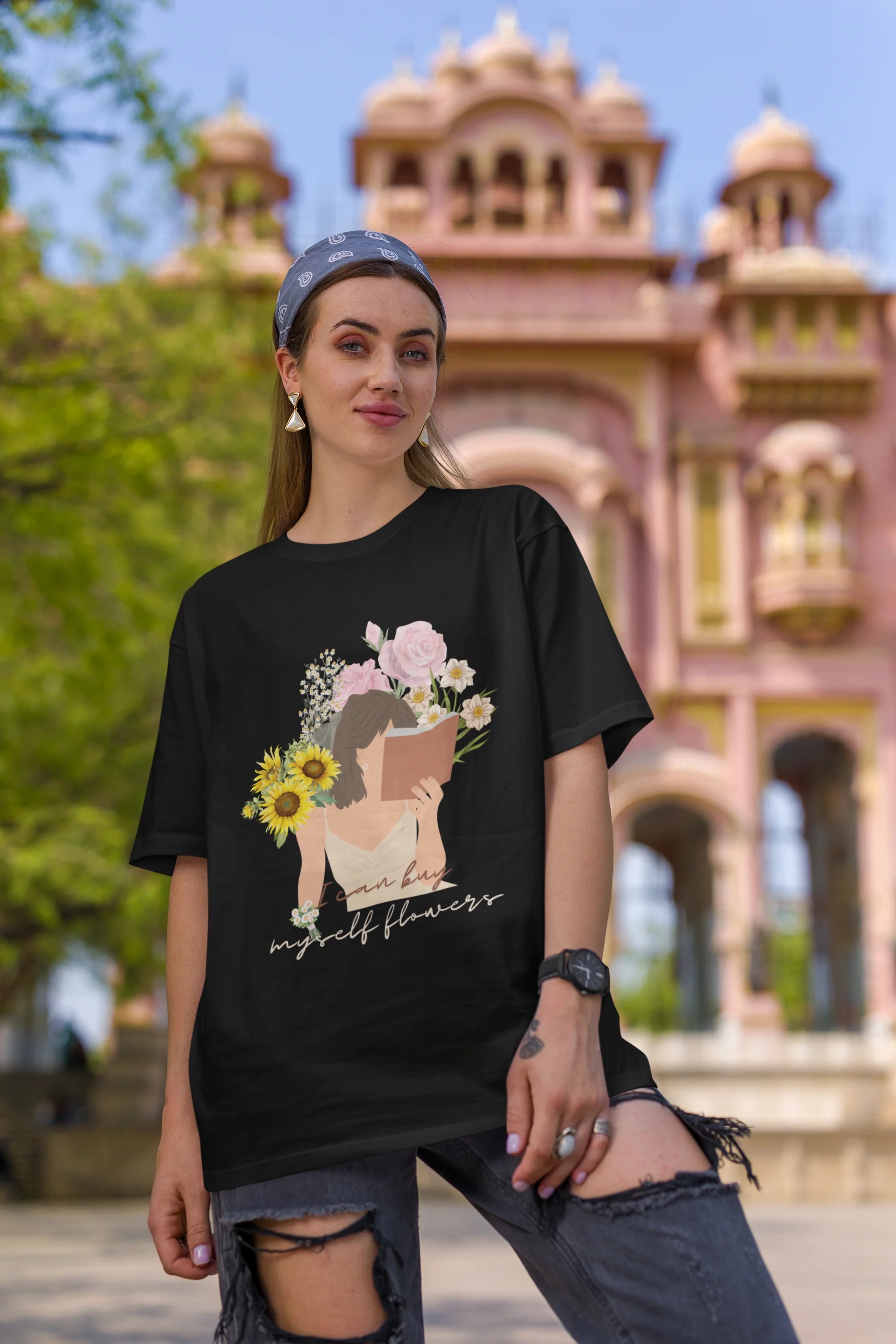 First front view of female model wearing a black oversized t-shirt with a positive message "Buy Myself Flowers" and a graphic of a smiling woman surrounded by tulips and sunflowers. Ideal for those who love inspirational clothing and floral designs.