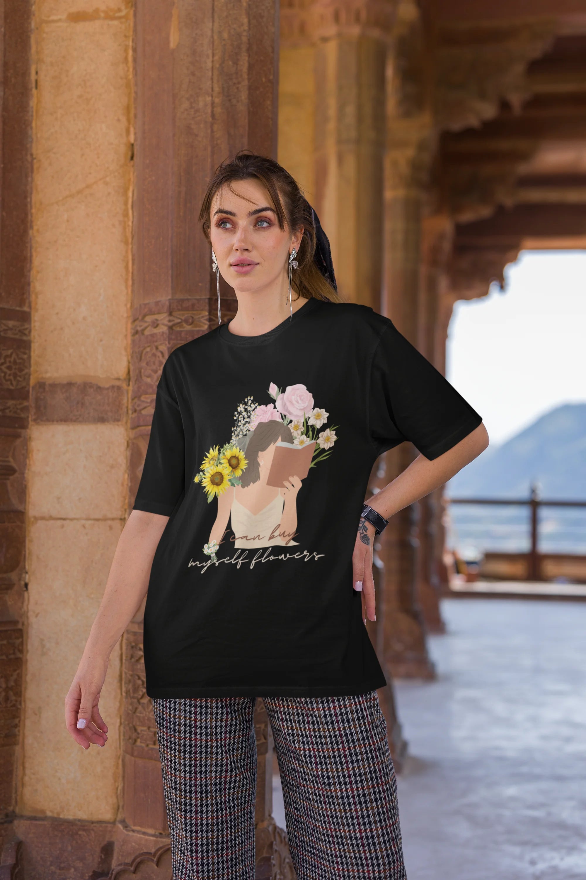 Third front view of female model wearing a black oversized t-shirt with a positive message "Buy Myself Flowers" and a graphic of a smiling woman surrounded by tulips and sunflowers. Ideal for those who love inspirational clothing and floral designs.