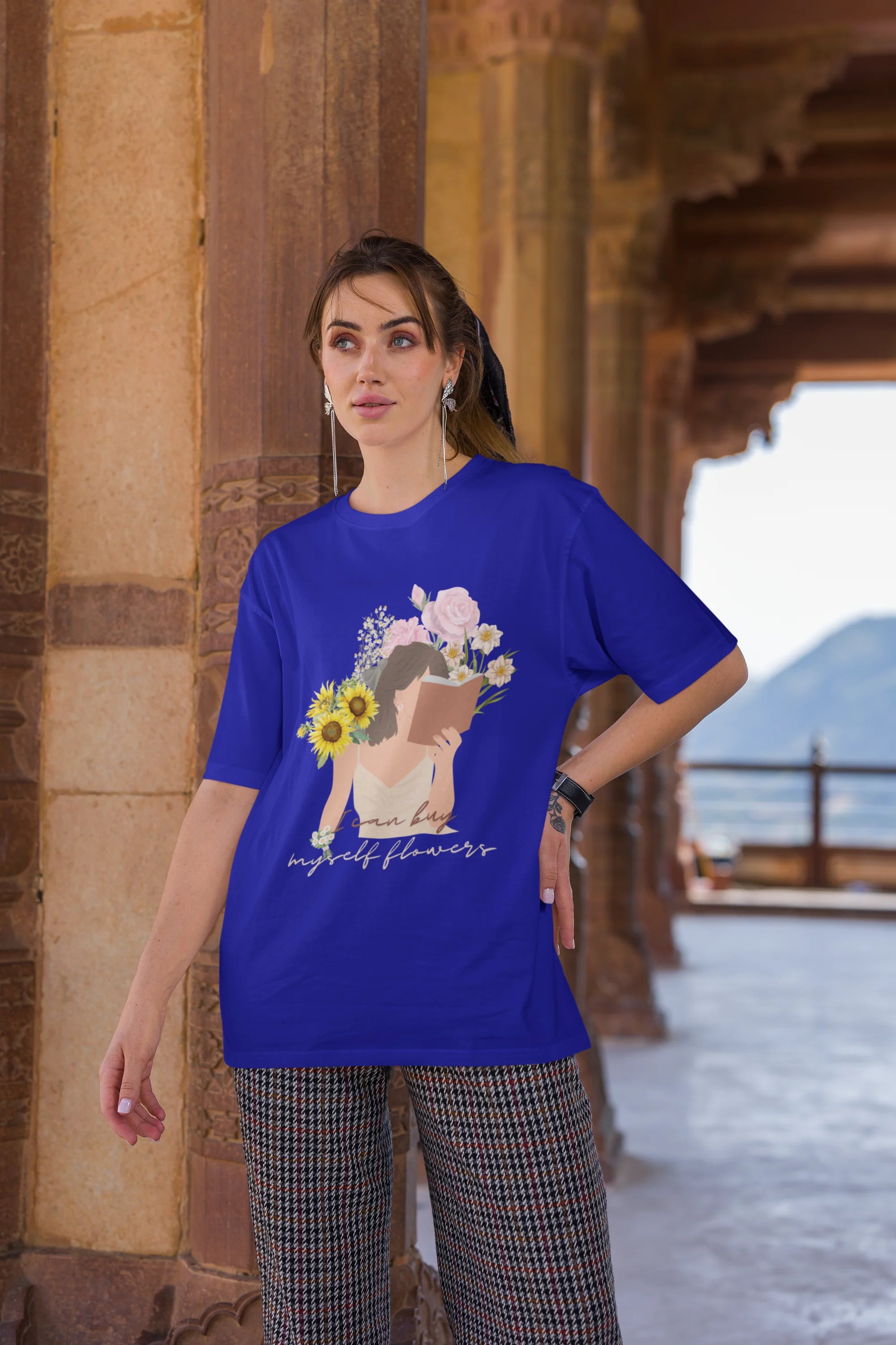 Third front view of female model wearing a royal blue oversized t-shirt with a positive message "Buy Myself Flowers" and a graphic of a smiling woman surrounded by tulips and sunflowers. Ideal for those who love inspirational clothing and floral designs.