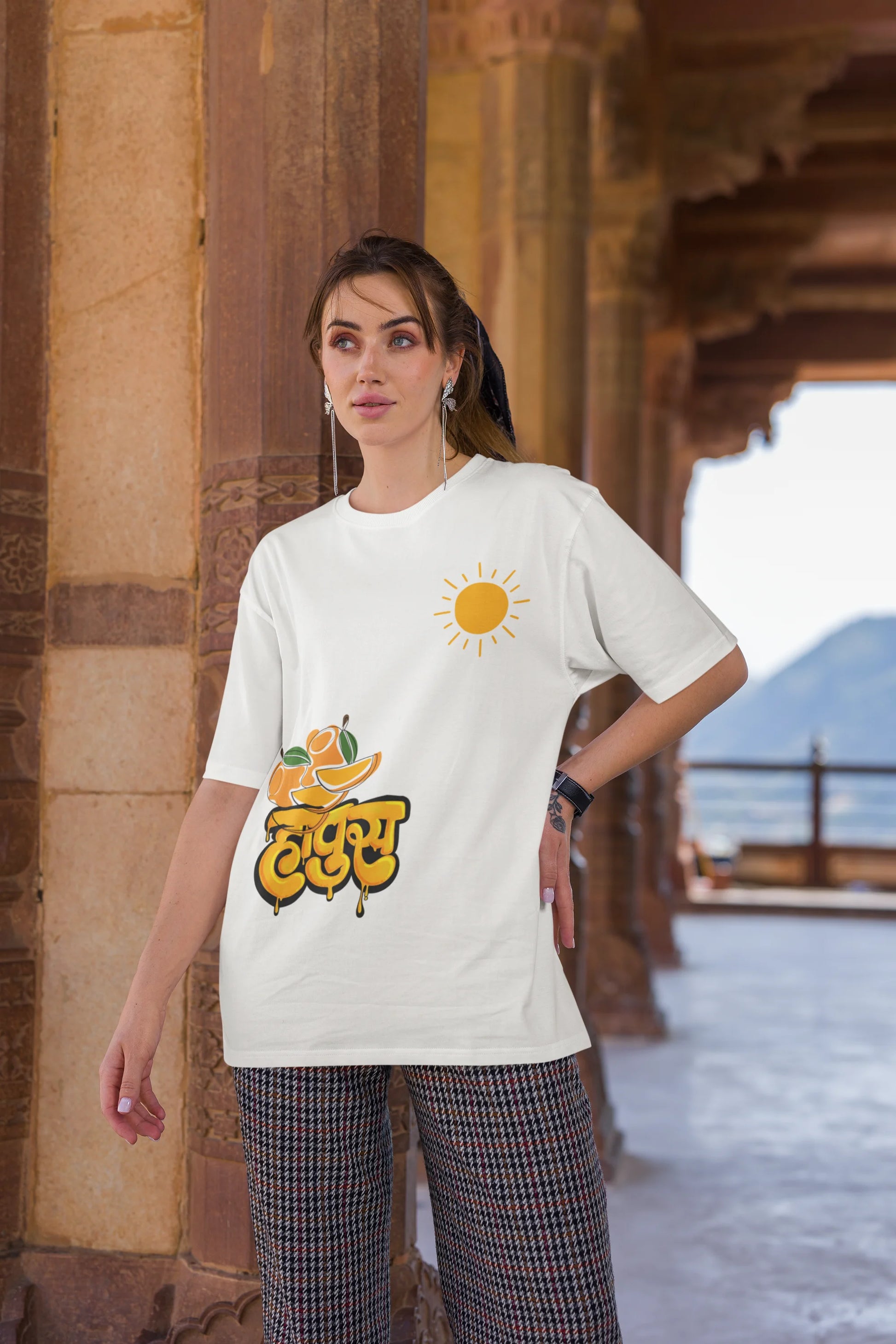 Third front view of female model wearing an off-white oversized t-shirt featuring a design inspired by the Marathi word "Hapus," meaning Alphonso mango. Ideal for fans of Marathi culture, foodies, and anyone who loves the king of fruits.
