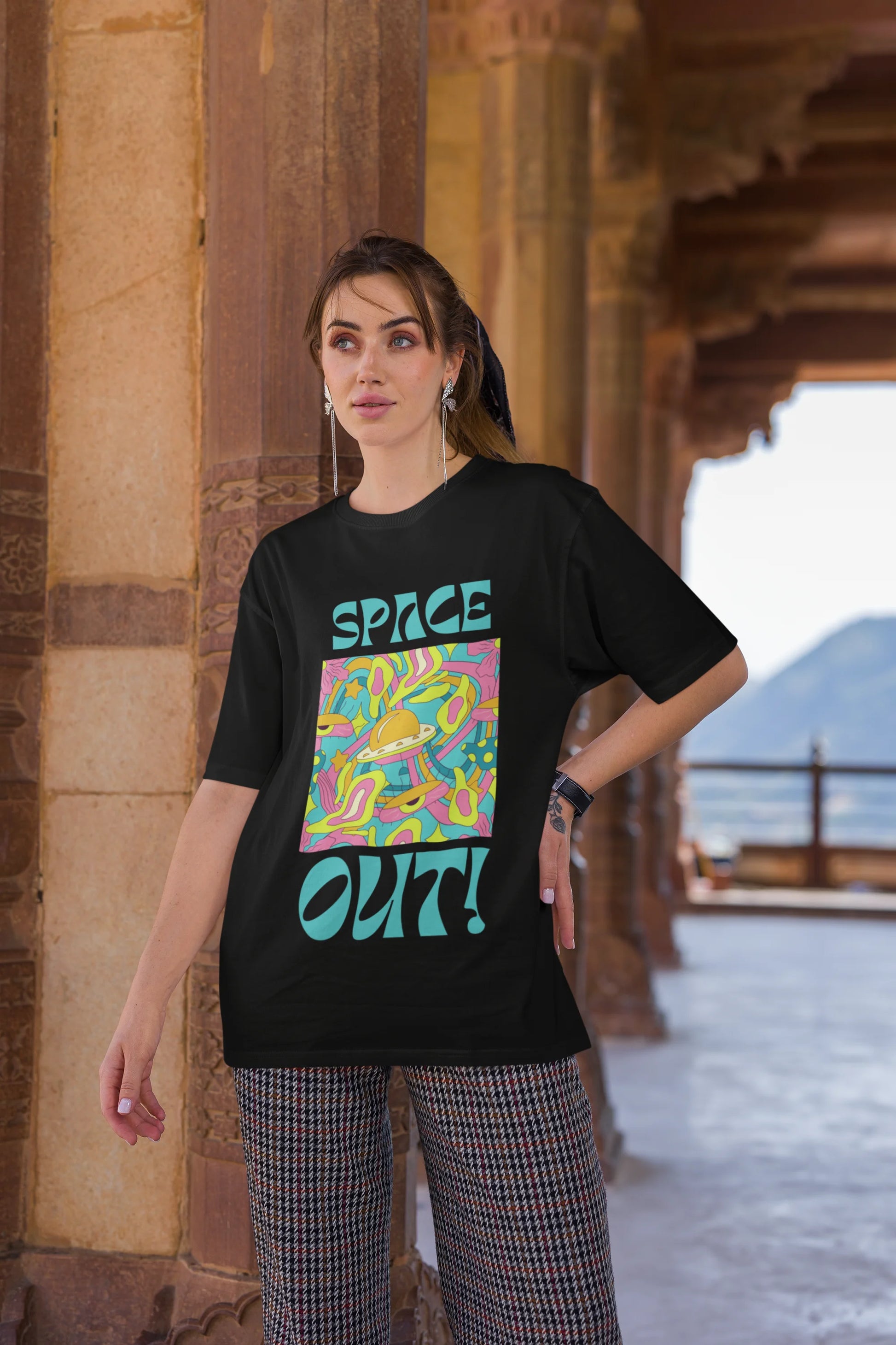 Third image of female model wearing an black oversized "Spaced Out" t-shirt featuring a vibrant color mashup design that evokes a sense of space exploration, playful aliens, and distant galaxies.