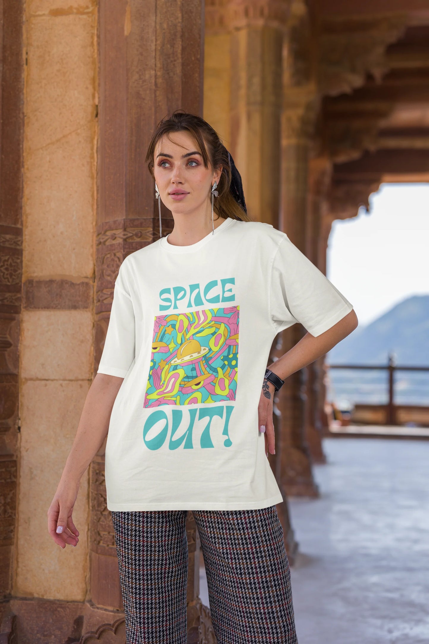 Third image of female model wearing an off white oversized "Spaced Out" t-shirt featuring a vibrant color mashup design that evokes a sense of space exploration, playful aliens, and distant galaxies.