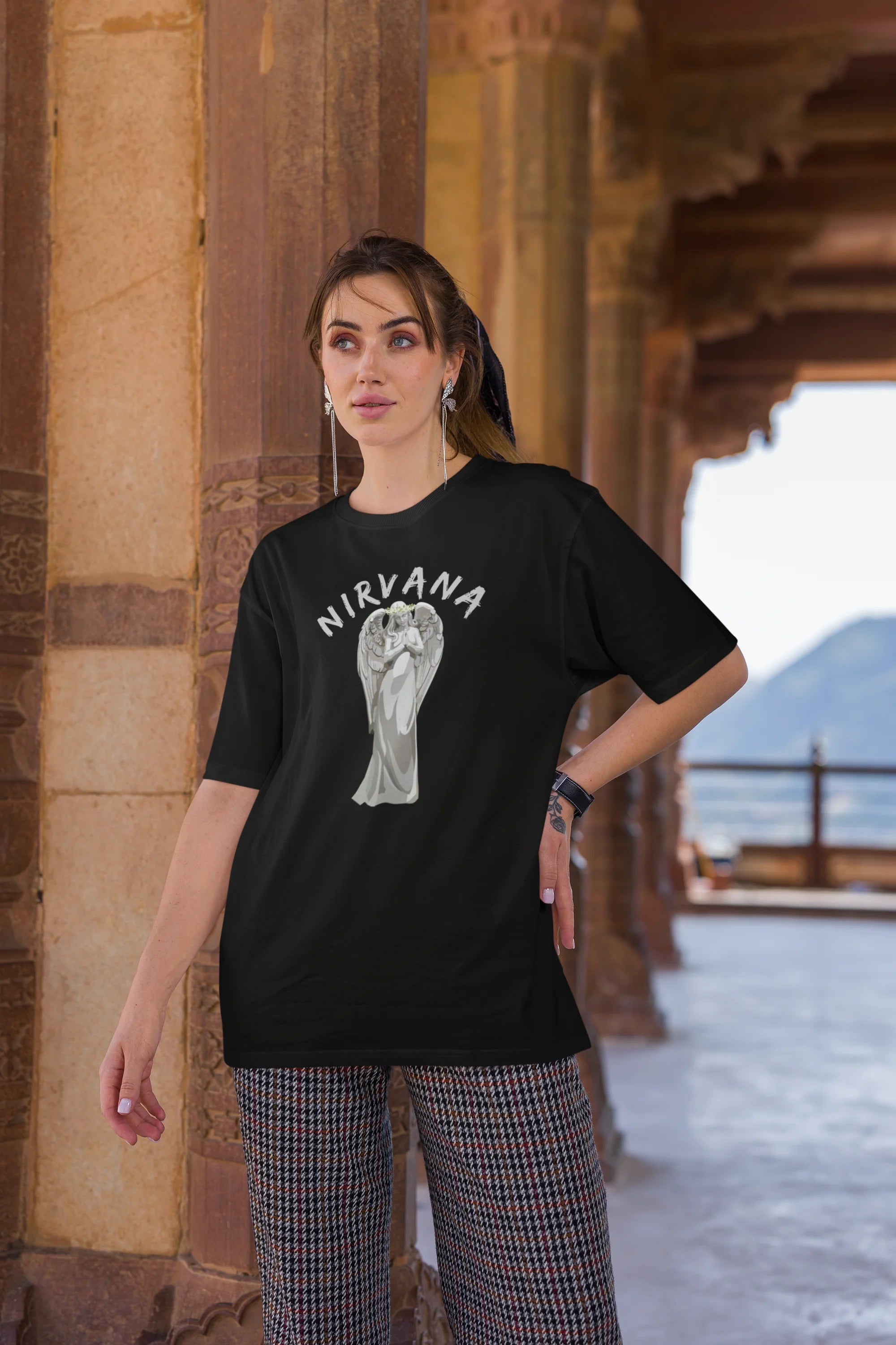 Third front image of female model wearing a black oversized t-shirt featuring a design of a winged angel with the text "Nirvana" above it. Ideal for fans of Nirvana and those who love grunge aesthetics.