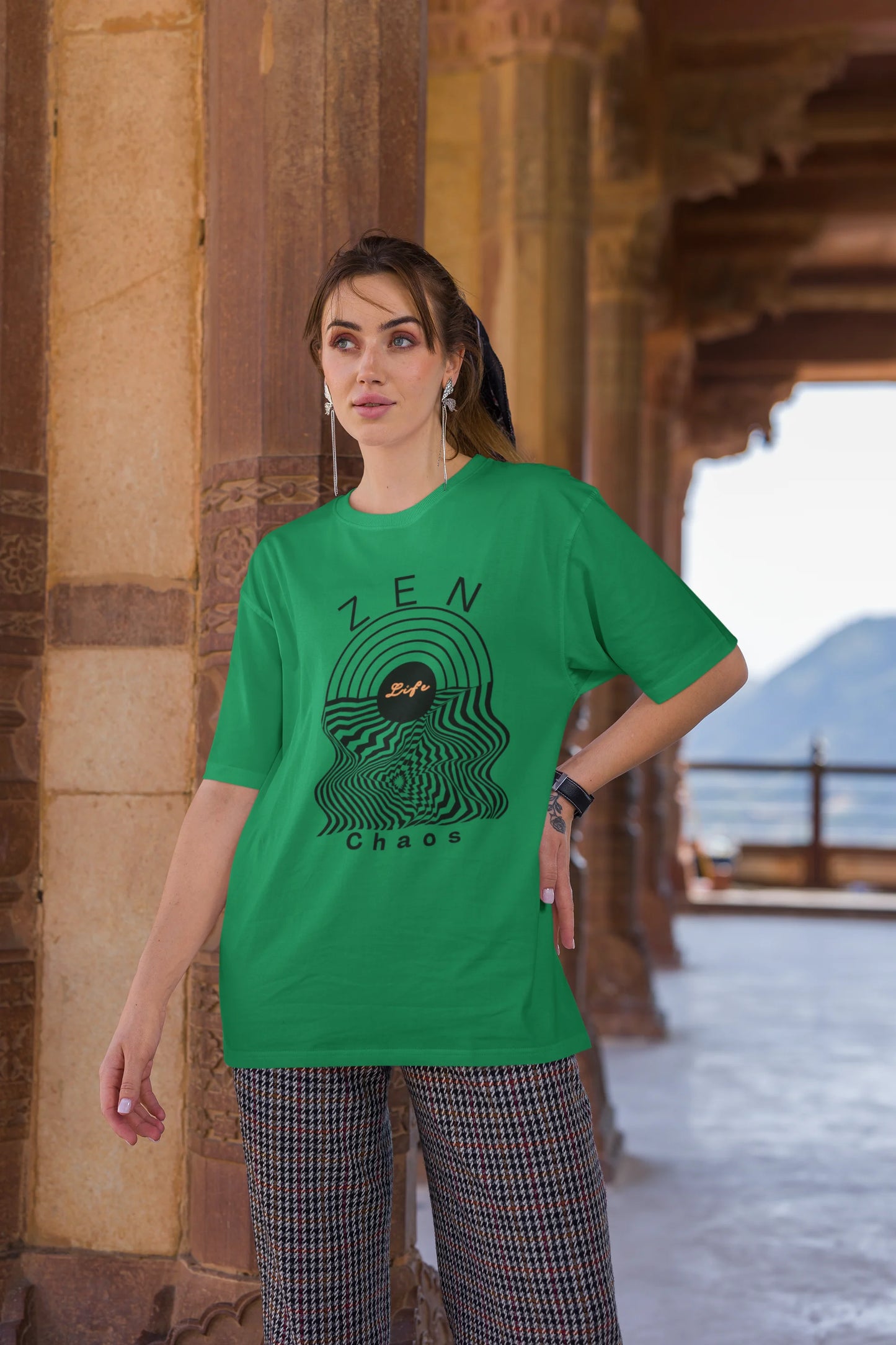 Third front view of a female model wearing an forest green oversized t-shirt featuring an aesthetic design of a setting sun and crashing waves with the text "Zen & Chaos" above it. Ideal for those who love philosophical themes and visually striking clothing.