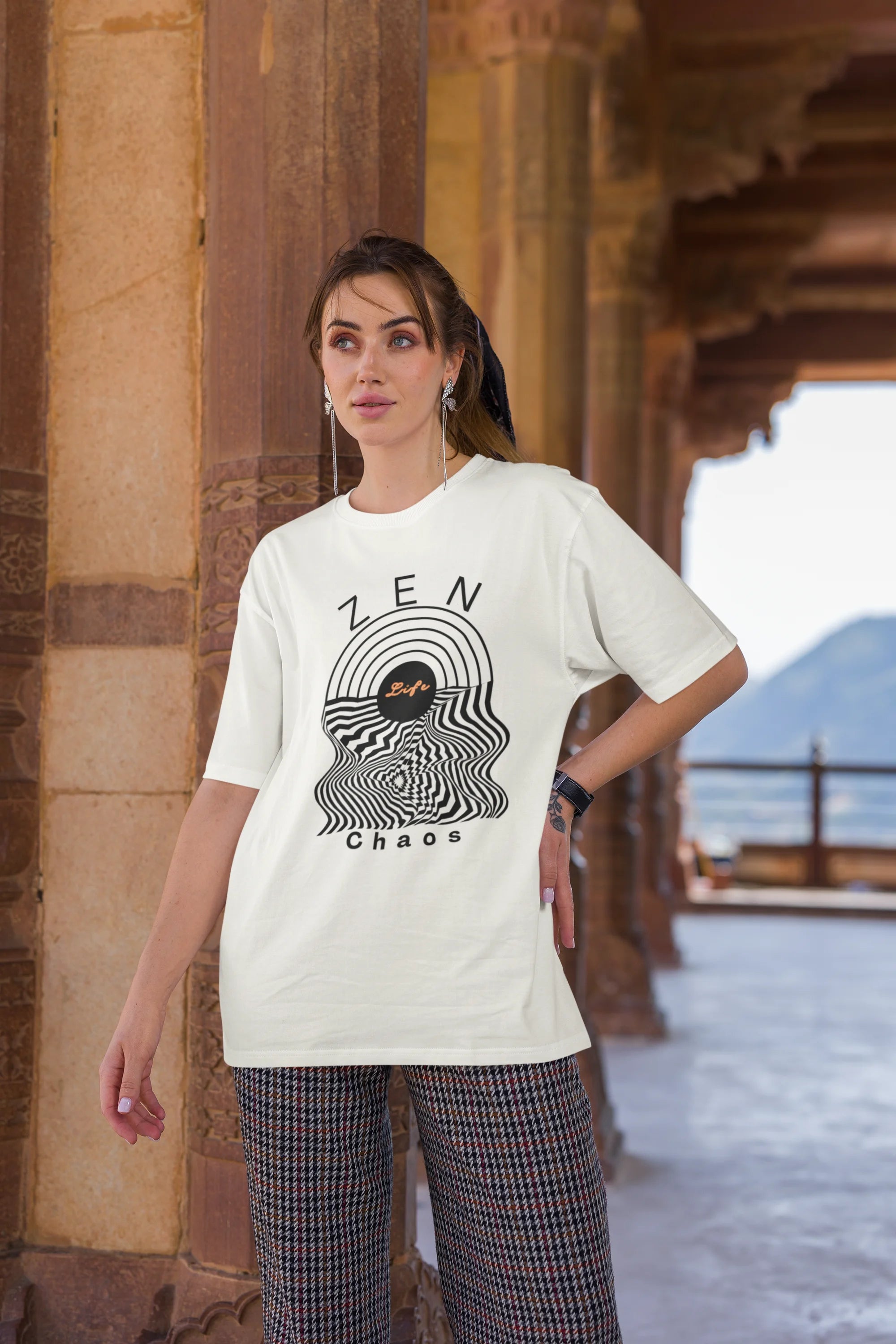 Third front image of a female model wearing an off-white oversized t-shirt featuring an aesthetic design of a setting sun and crashing waves with the text "Zen & Chaos" above it. Ideal for those who love philosophical themes and visually striking clothing.