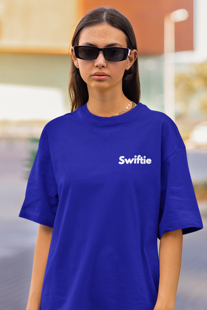 Close up front view of female model flaunting Taylor Swift-themed blue oversized tee, epitomizing rockstar chic with nods to Taylor's Version and Eras Tour.