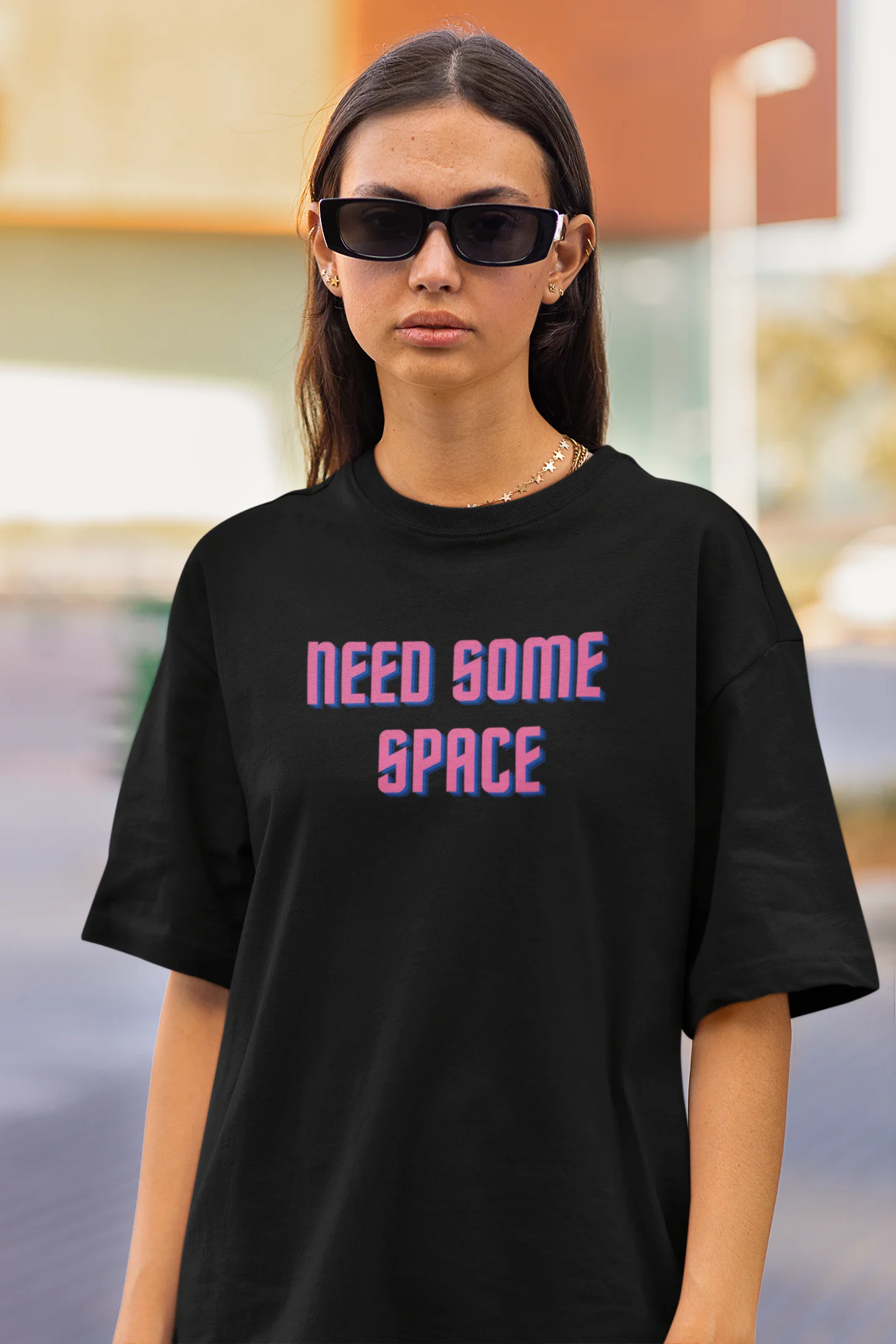 Closeup front view of a female model wearing a black oversized t-shirt with a bold graphic that reads "Need Some Space" on the front. The design incorporates subtle hints of the Milky Way galaxy and the solar system on the back.