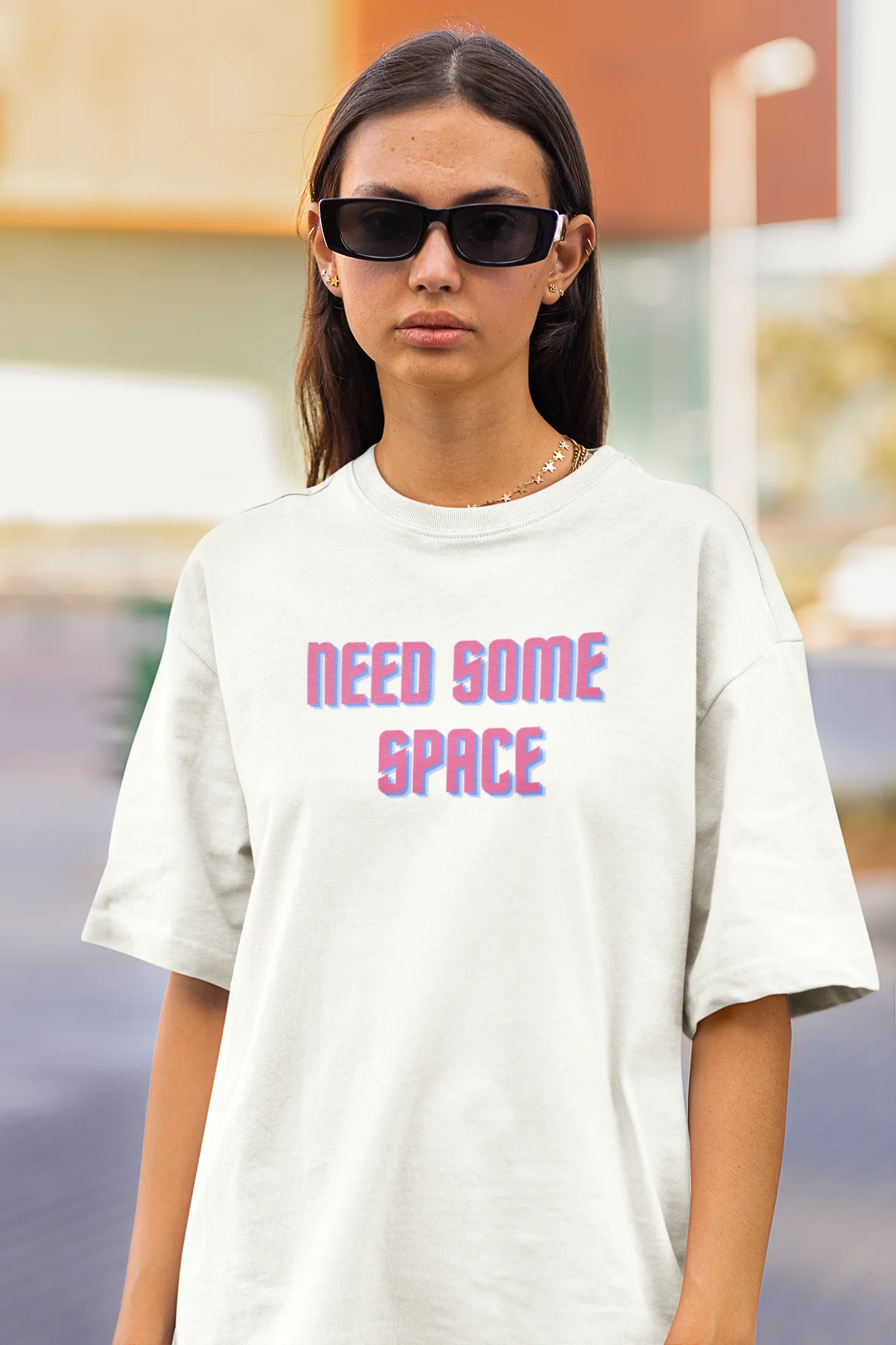 Closeup front view of a female model wearing a white oversized t-shirt with a bold graphic that reads "Need Some Space" on the front. The design incorporates subtle hints of the Milky Way galaxy and the solar system on the back.