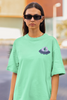 Close up front view of a female model wearing a mint green oversized t-shirt featuring a fun 