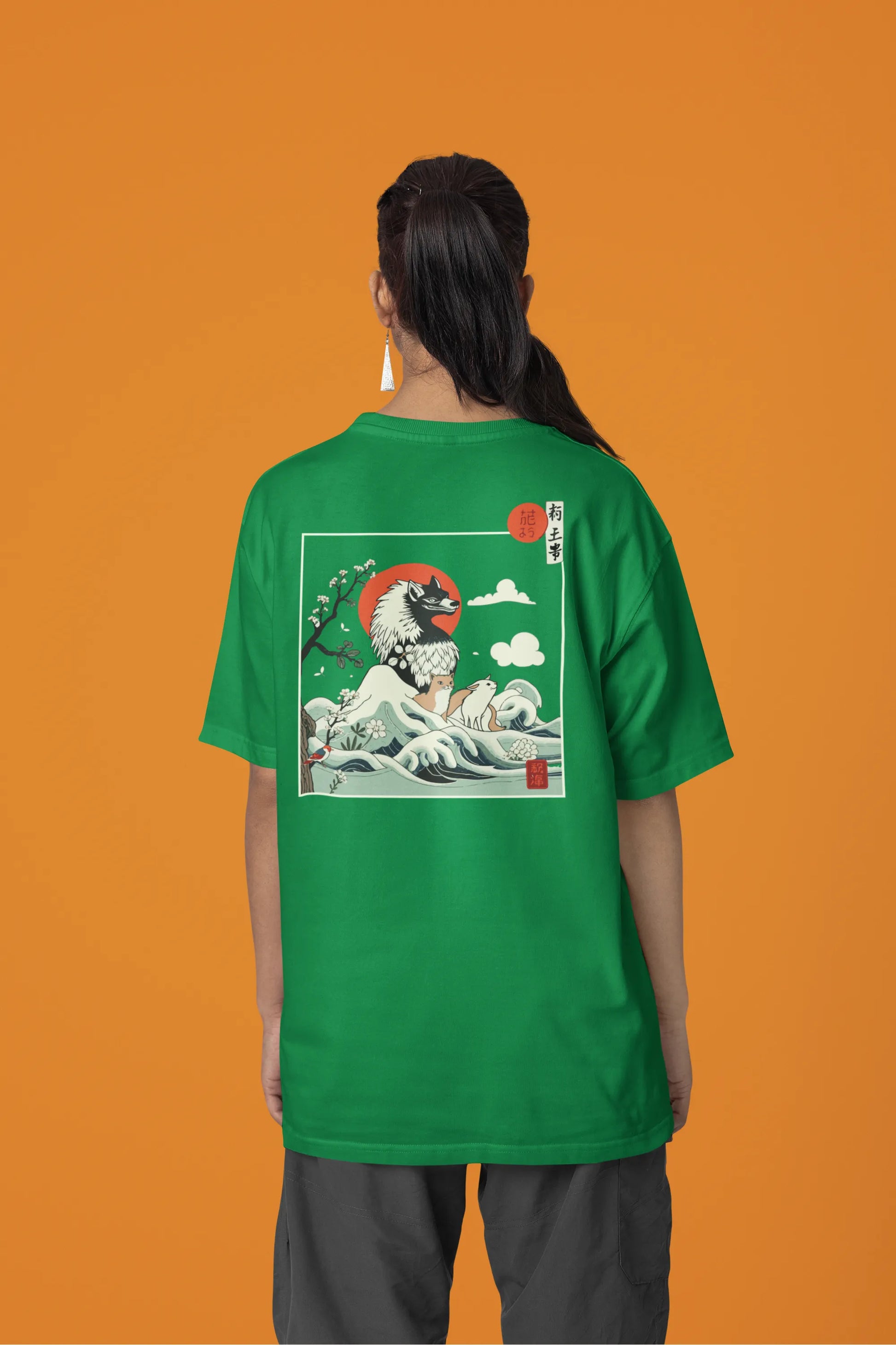 Back view of a female model wearing a forest green oversized tee with a design of a wolf surveying a Japanese landscape.