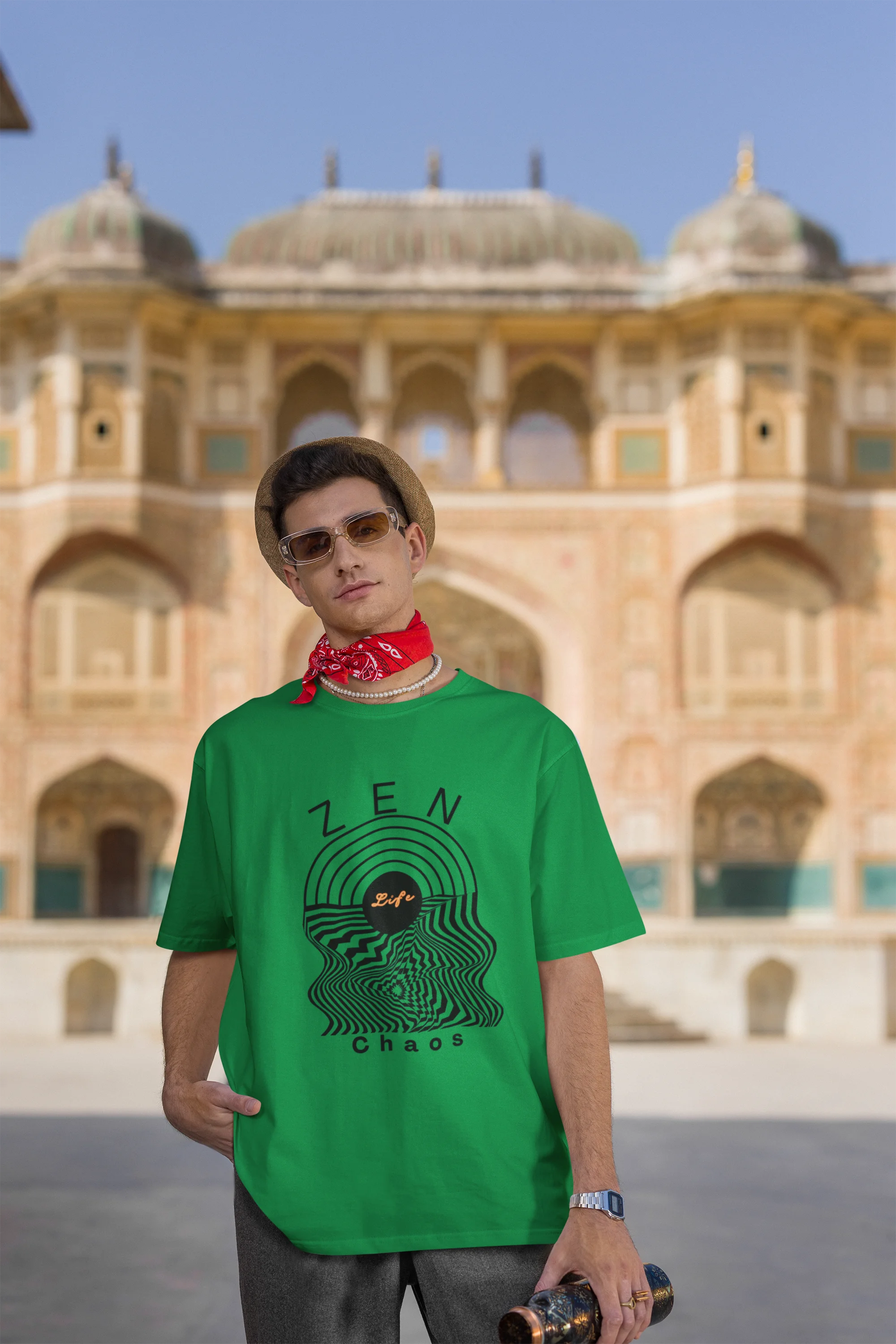 Third front view of a male model wearing an forest green oversized t-shirt featuring an aesthetic design of a setting sun and crashing waves with the text "Zen & Chaos" above it. Ideal for those who love philosophical themes and visually striking clothing.