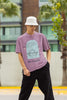 Front view of a male model wearing a dirty purple oversized t-shirt with a beautiful outline of the sun setting into the sea, offering a serene and coastal aesthetic.