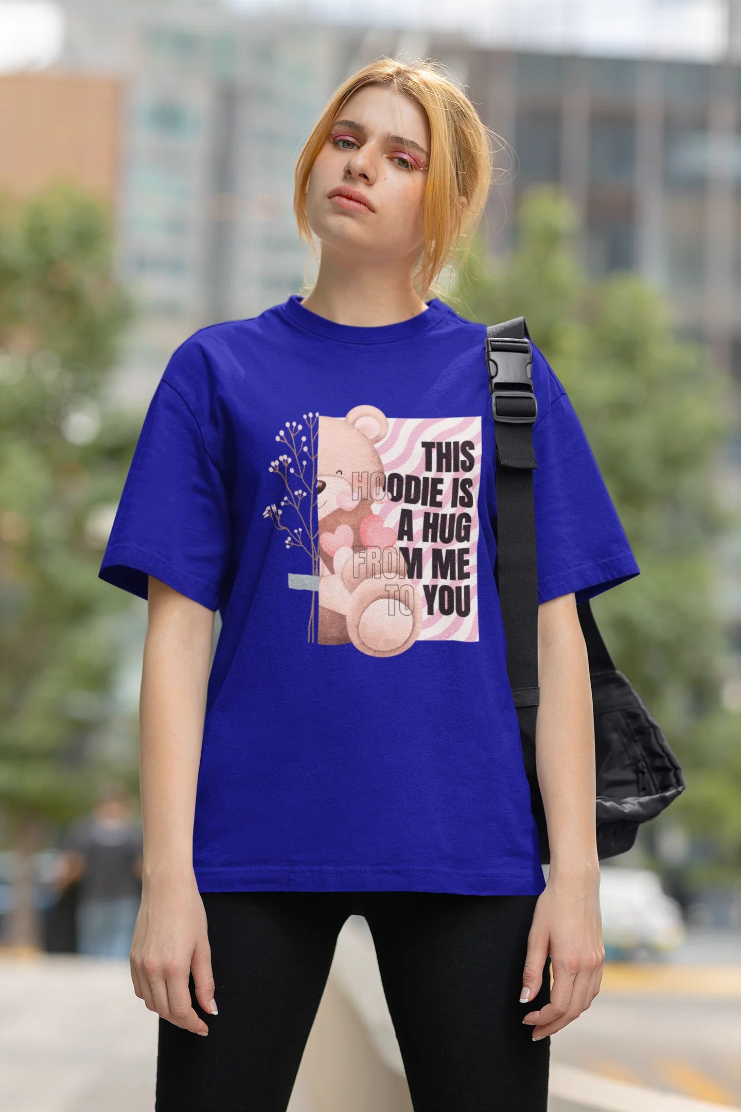 Third front view of a female model wearing an royal blue oversized t-shirt with a heartwarming design of a teddy bear offering a hug, offering a comforting and relaxing aesthetic.