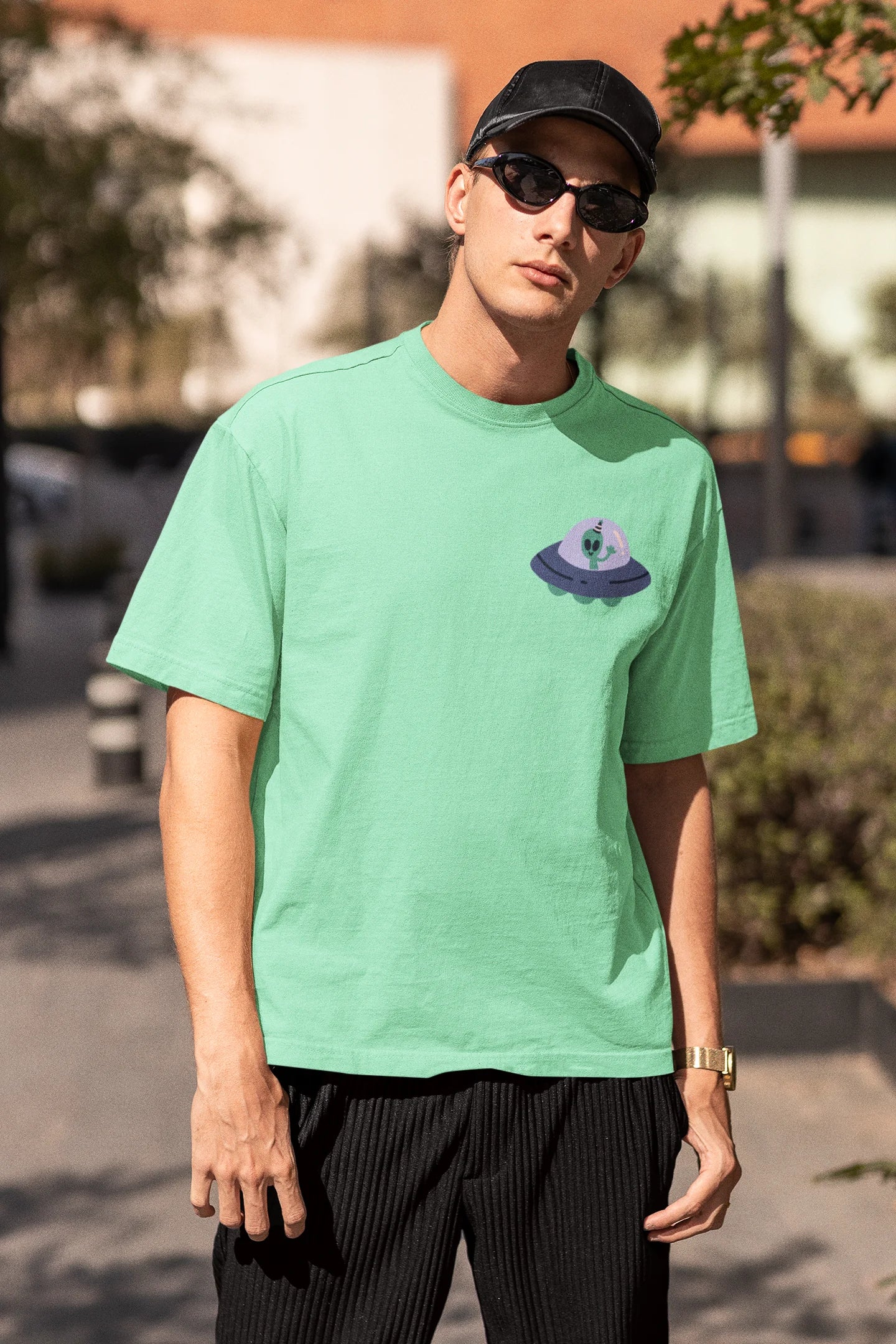 Third front view of a male model wearing a mint green oversized t-shirt featuring a fun "Alienated" design with elements of spaceships, UFOs, and a hint of extraterrestrial life.