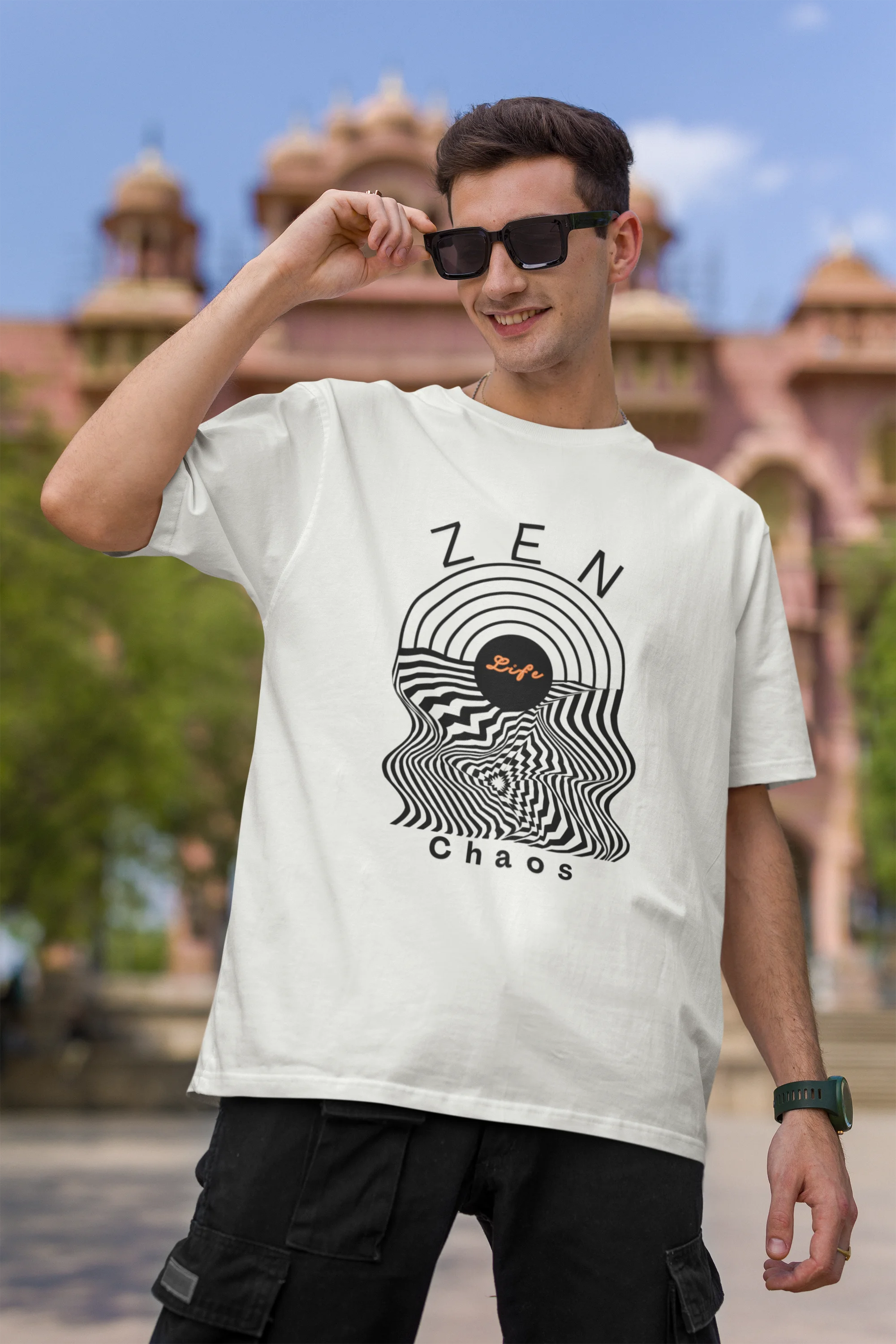 First front image of a male model wearing an off-white oversized t-shirt featuring an aesthetic design of a setting sun and crashing waves with the text "Zen & Chaos" above it. Ideal for those who love philosophical themes and visually striking clothing.