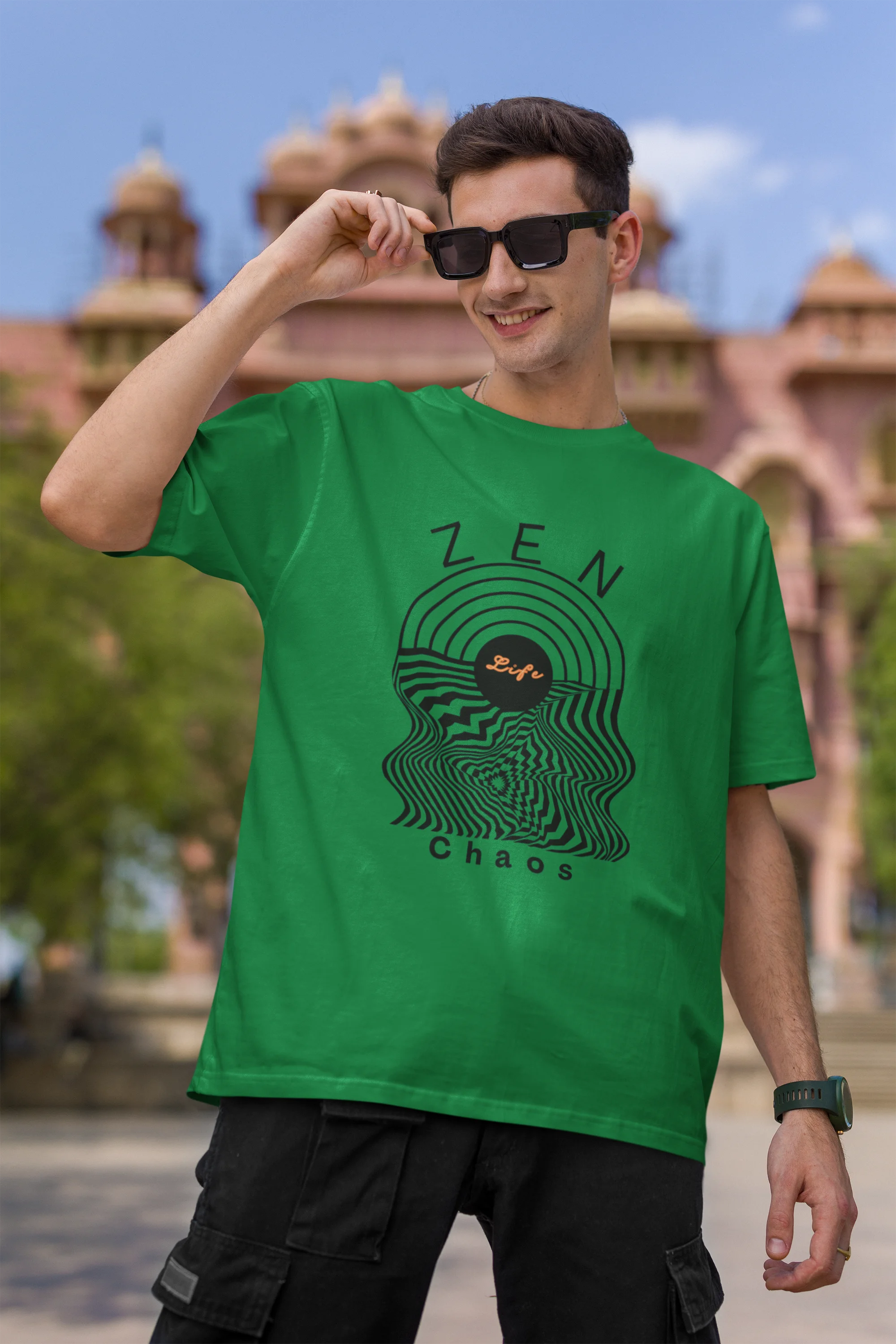 First front view of a male model wearing an forest green oversized t-shirt featuring an aesthetic design of a setting sun and crashing waves with the text "Zen & Chaos" above it. Ideal for those who love philosophical themes and visually striking clothing.