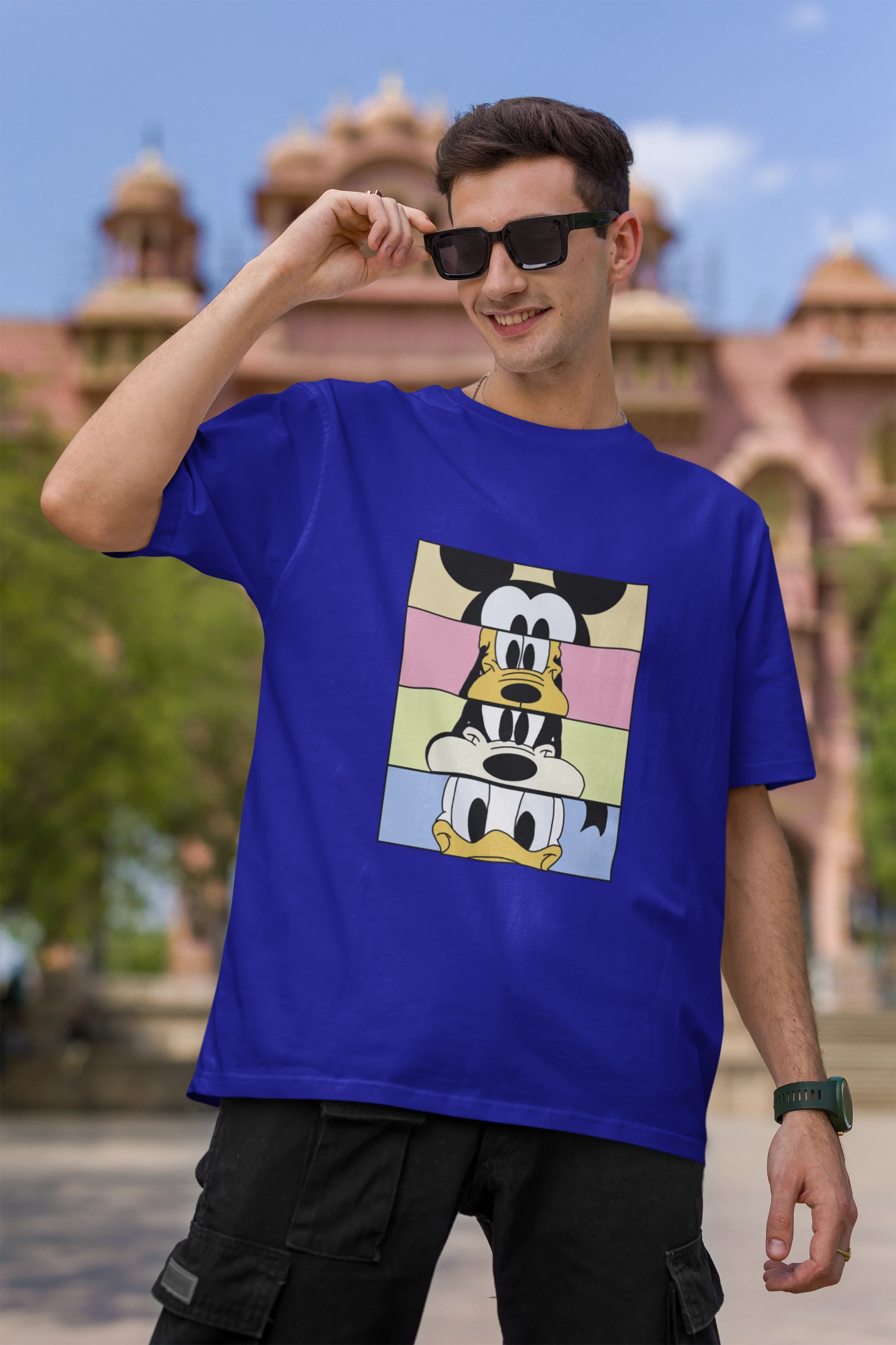 First image of male Model showcasing blue oversized t-shirt inspired by Mickey Mouse Clubhouse characters: Mickey Mouse, Donald Duck, Goofy, and Minnie Mouse