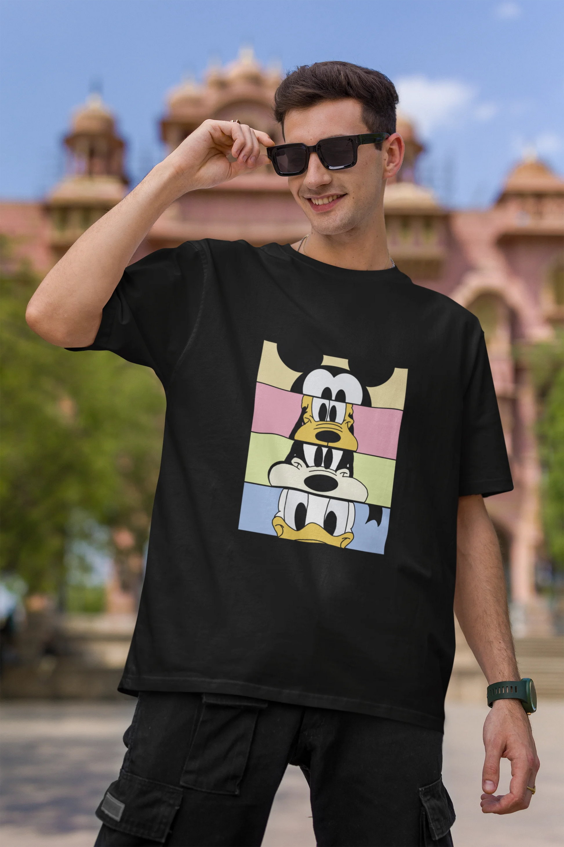 First image of male Model showcasing black oversized t-shirt inspired by Mickey Mouse Clubhouse characters: Mickey Mouse, Donald Duck, Goofy, and Minnie Mouse